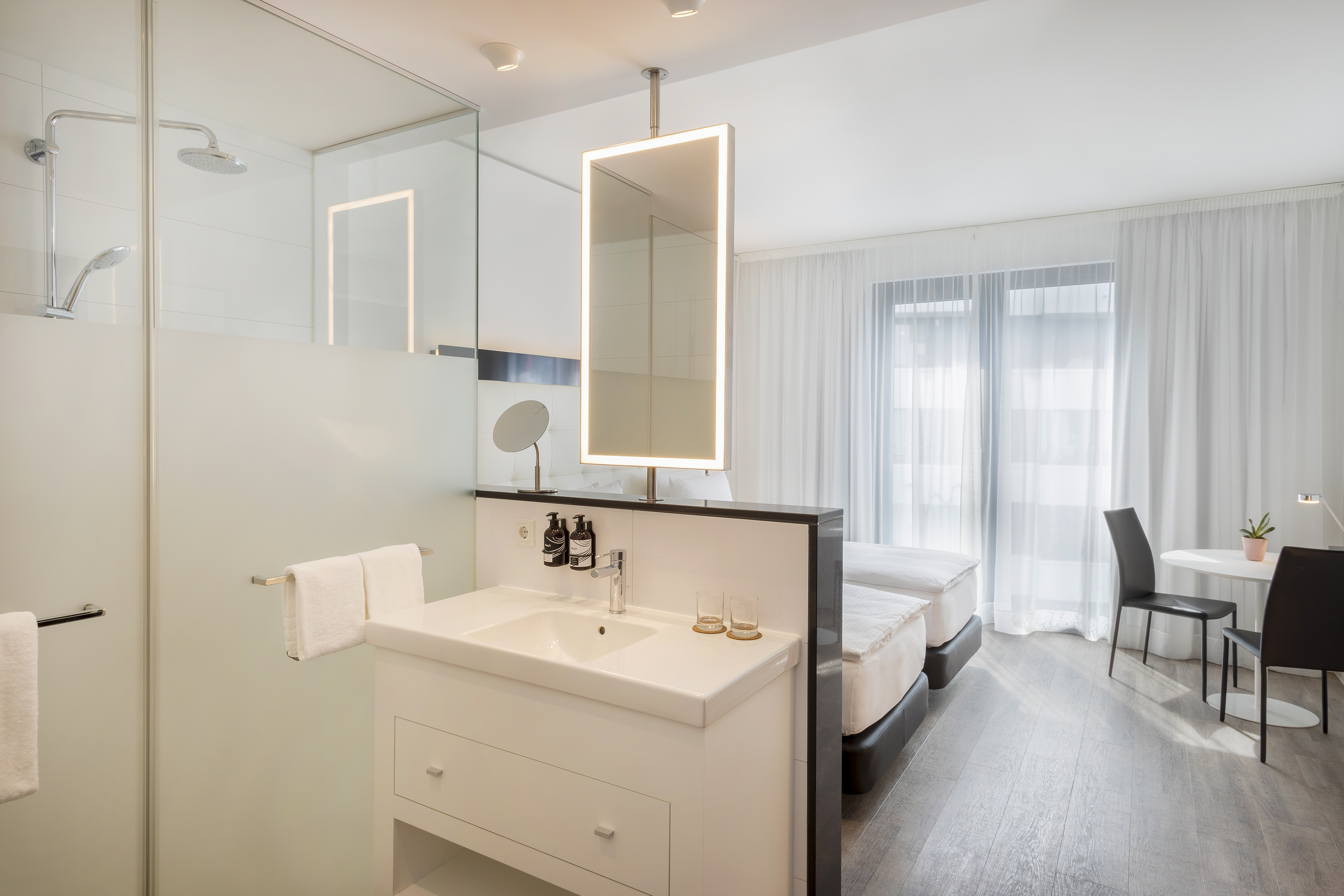 Sleek hotel room with open-concept bathroom, twin beds, and modern furnishings.