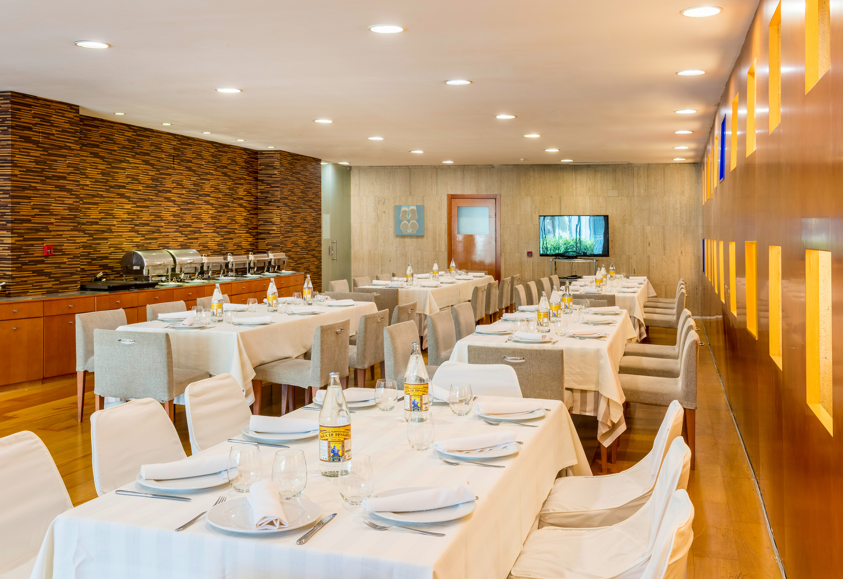 Modern hotel restaurant with set tables, buffet, and wood accent walls.