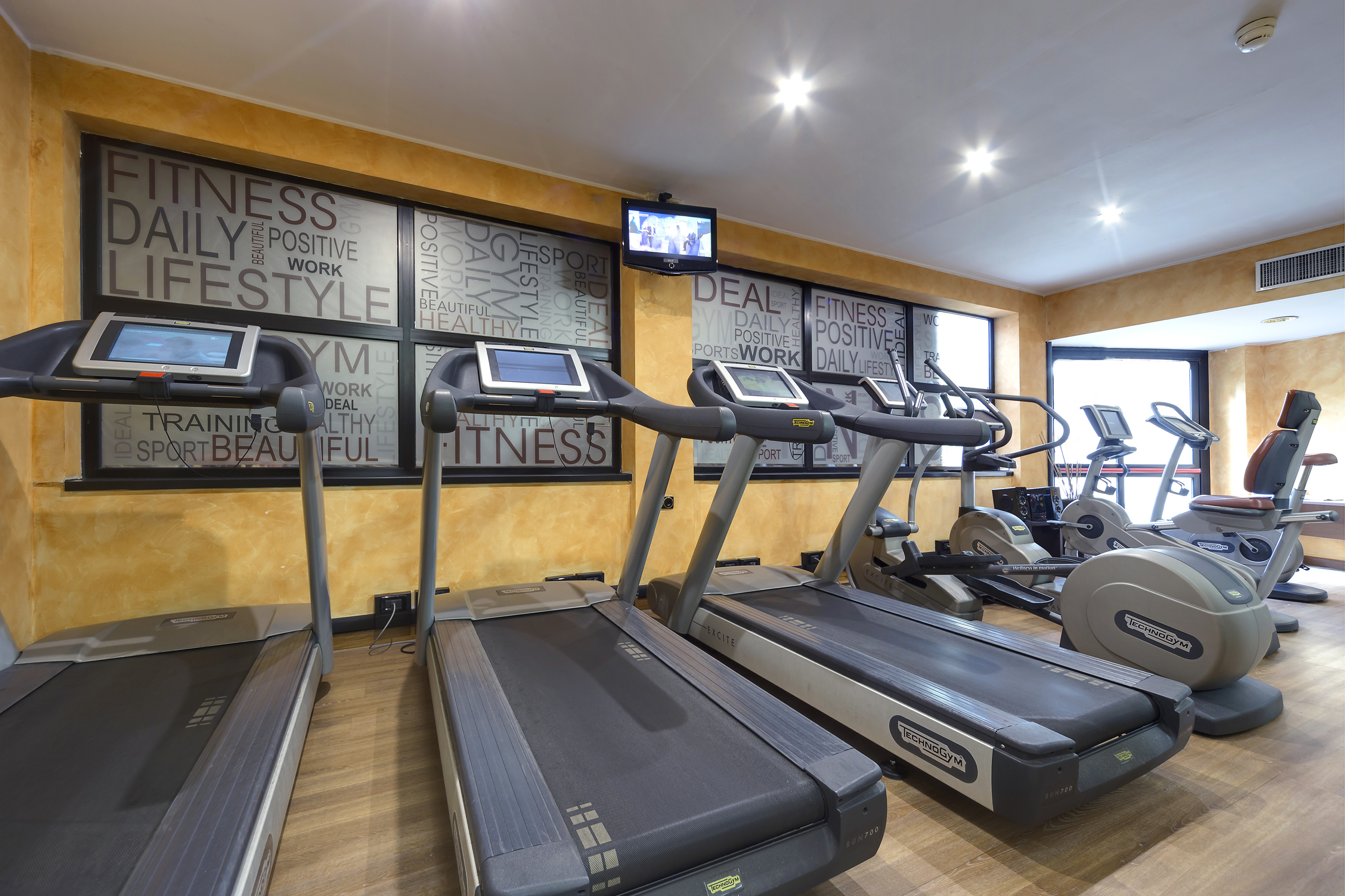 Modern hotel gym with Technogym treadmills, elliptical, and recumbent bike.