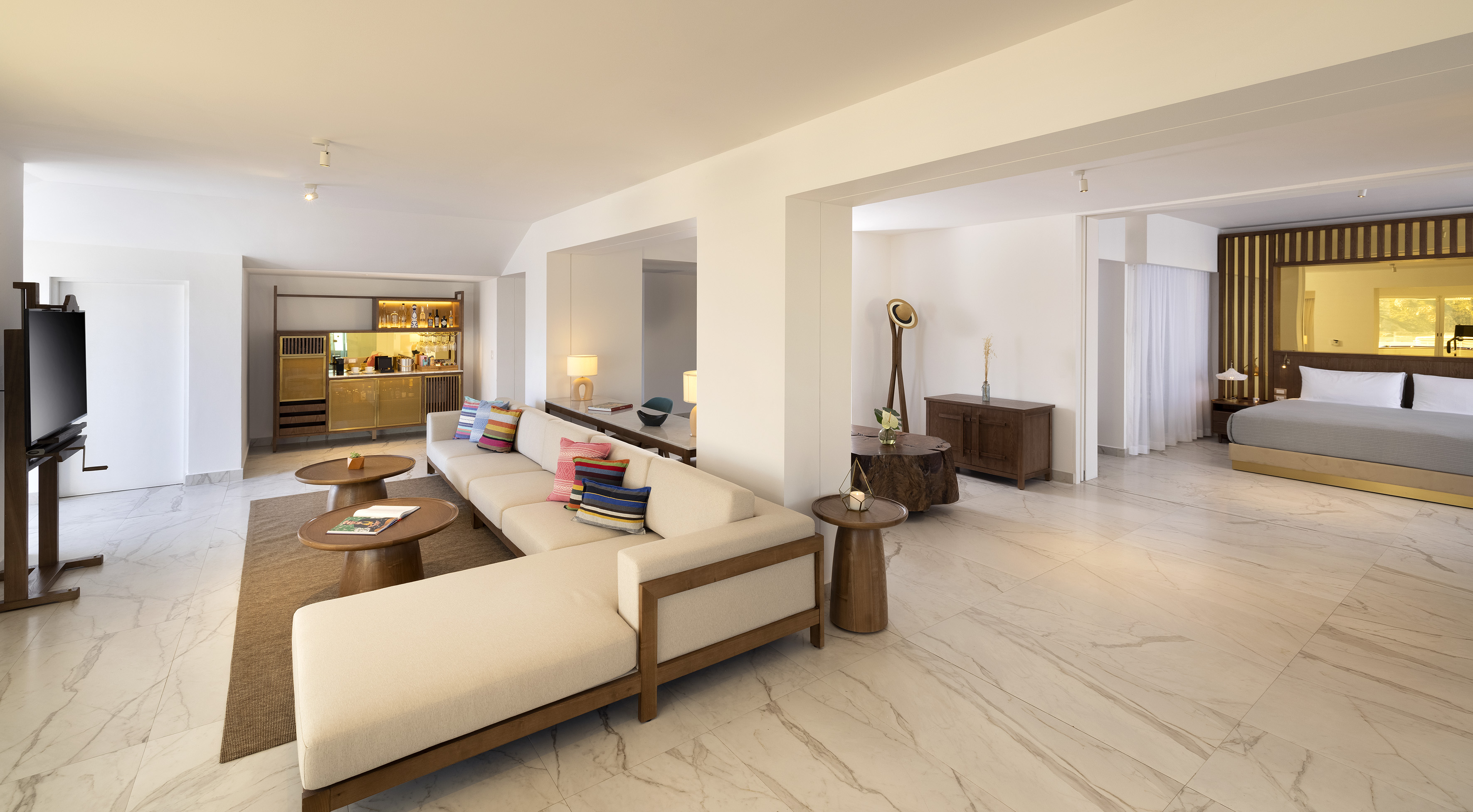Modern open-plan hotel suite with living room, minibar, and connected bedroom.