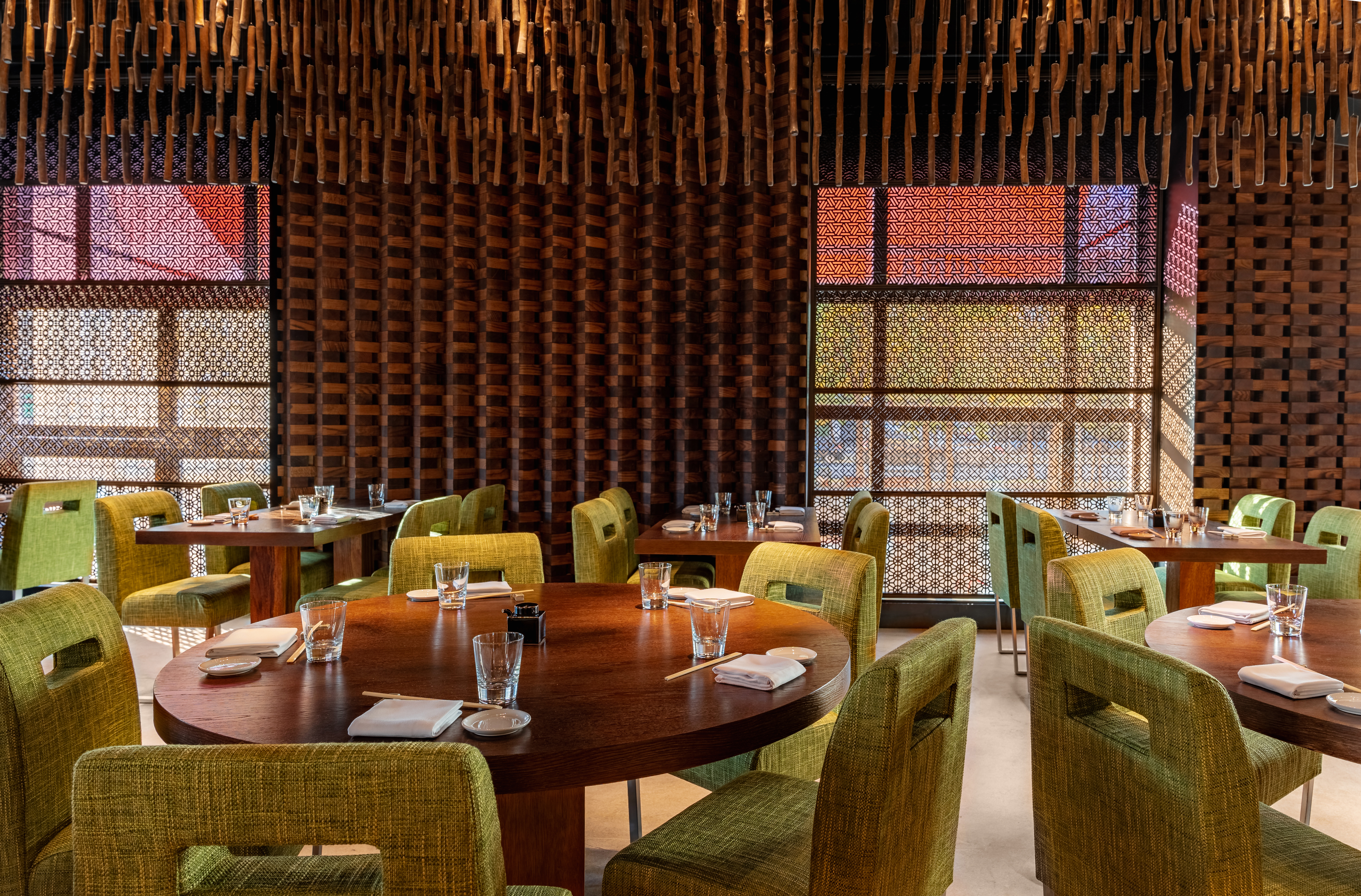 Modern restaurant with intricate wood decor, green chairs, and patterned screens.