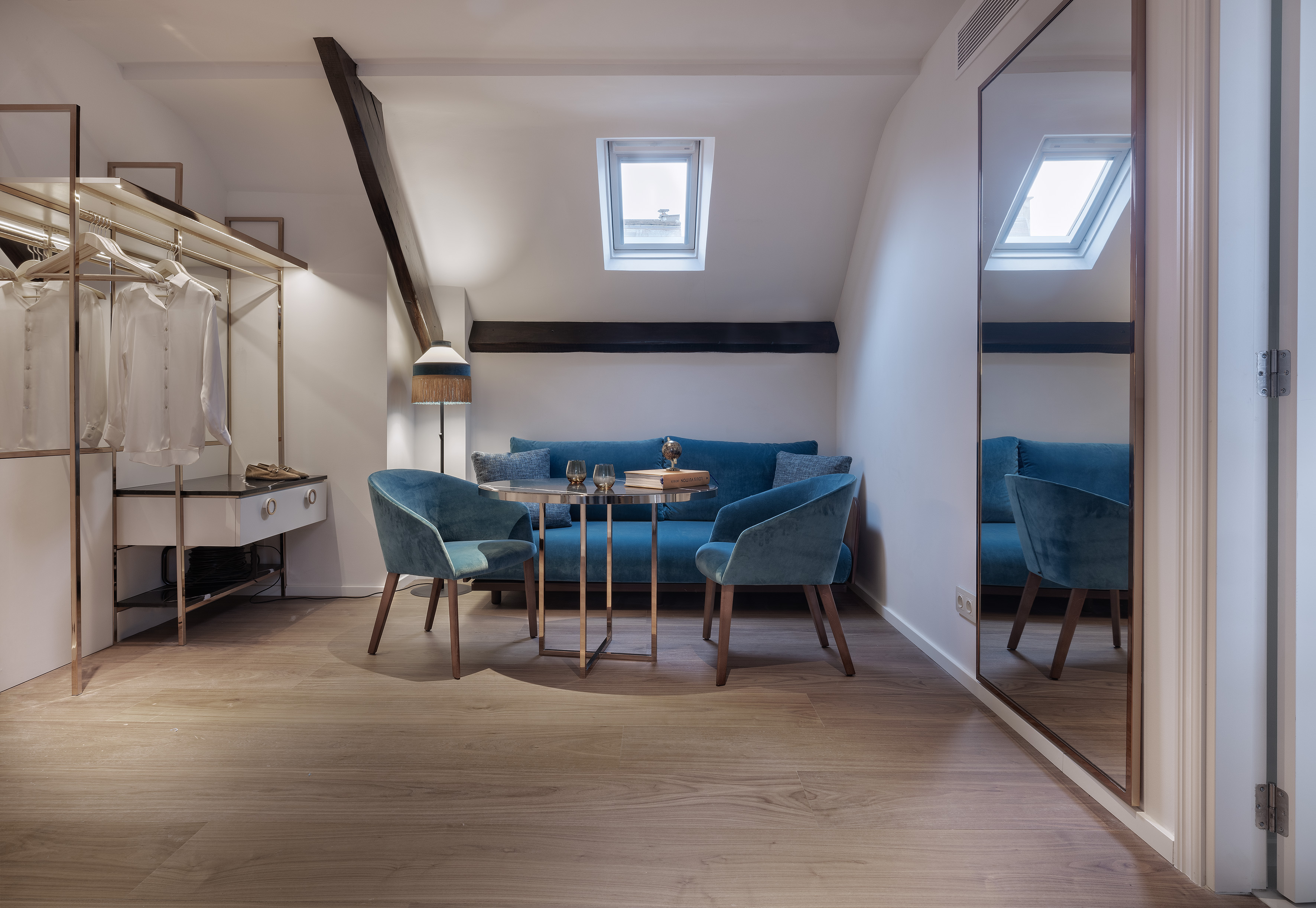 Modern attic living area with blue sofa, armchairs, skylight, and wardrobe.