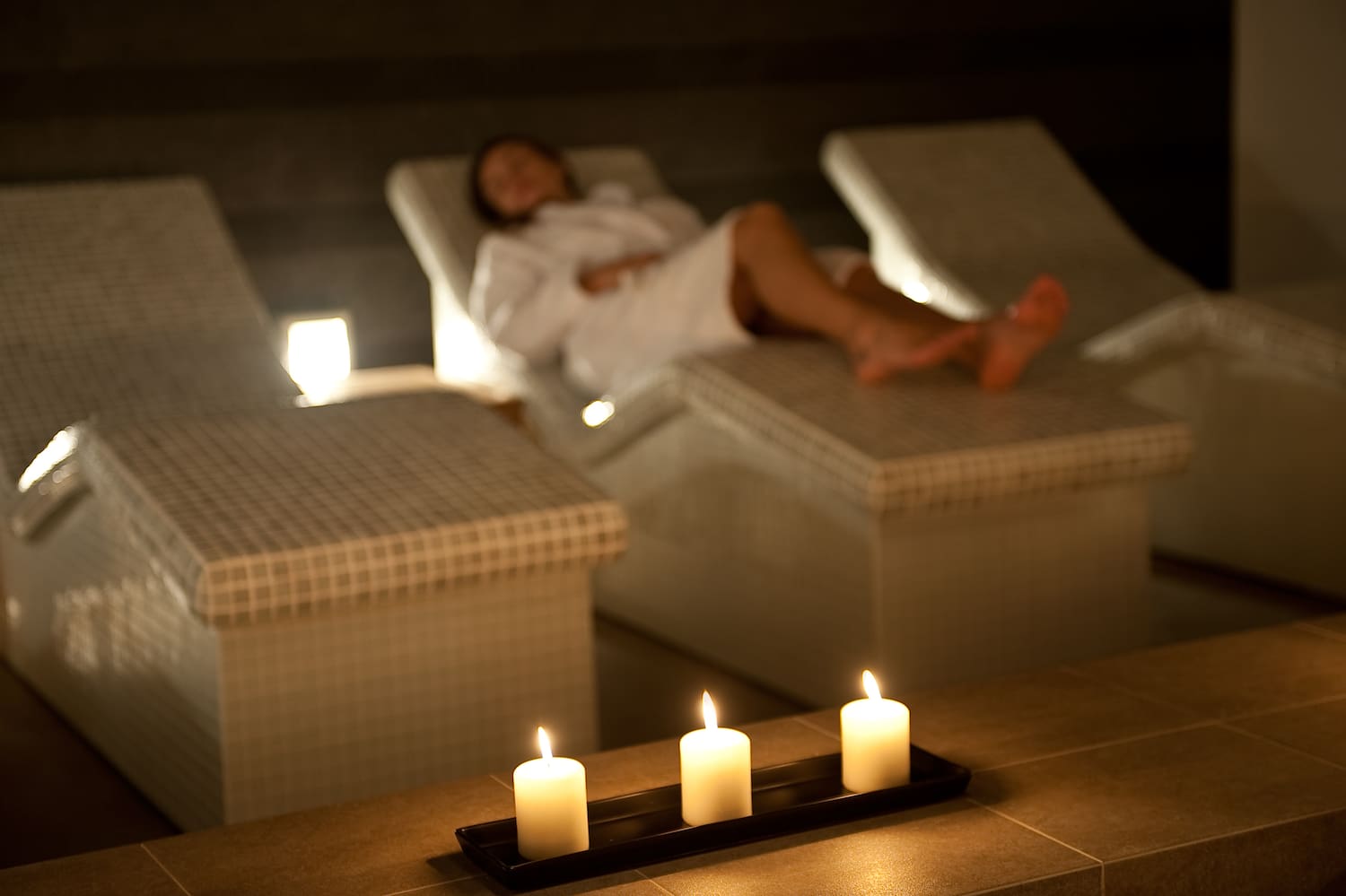 a woman lying on a lounge chair with candles in the background