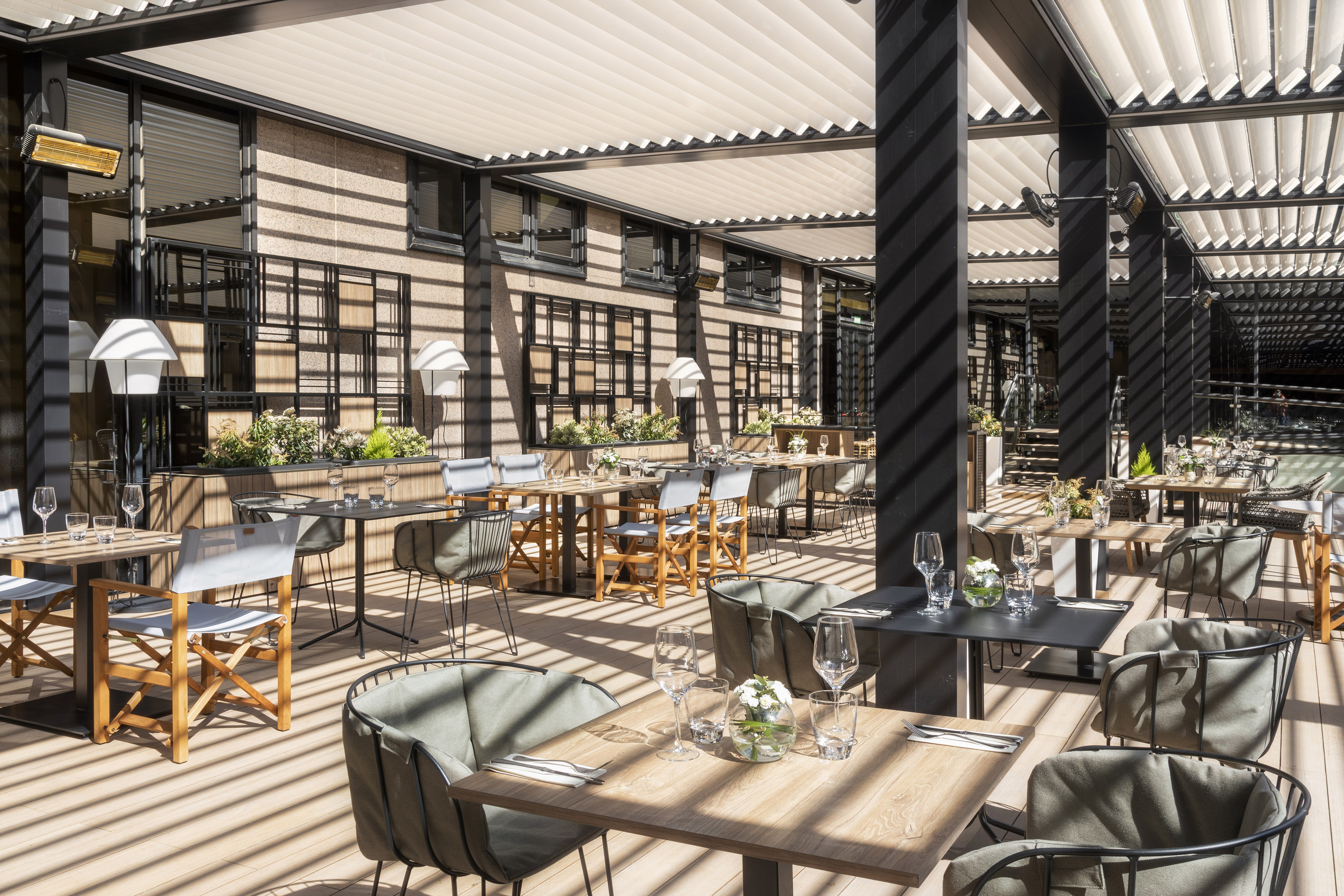Modern restaurant terrace with dining tables under a retractable pergola.