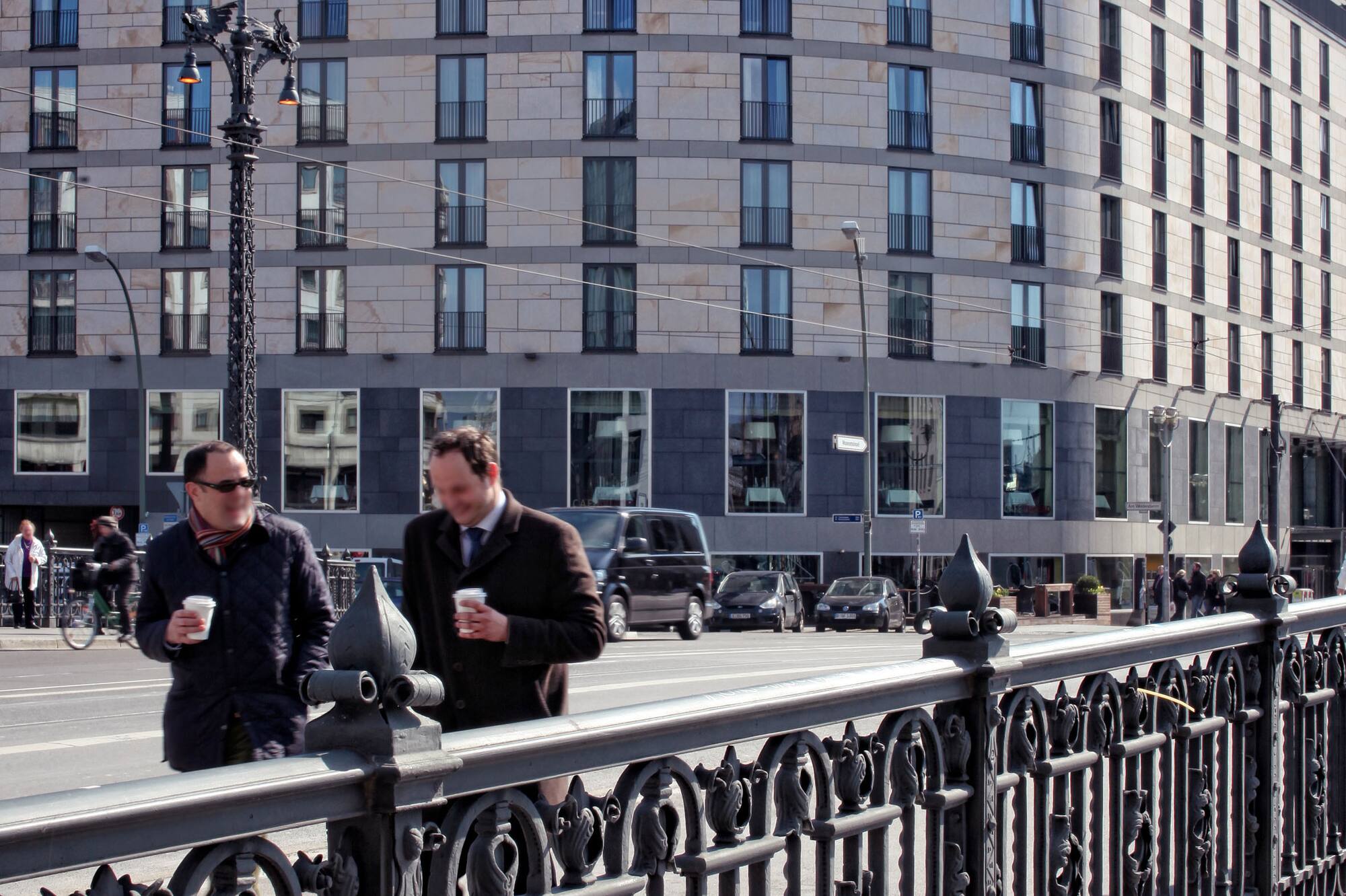 Urban street with Melia Hotel, two men, and ornate black railing.