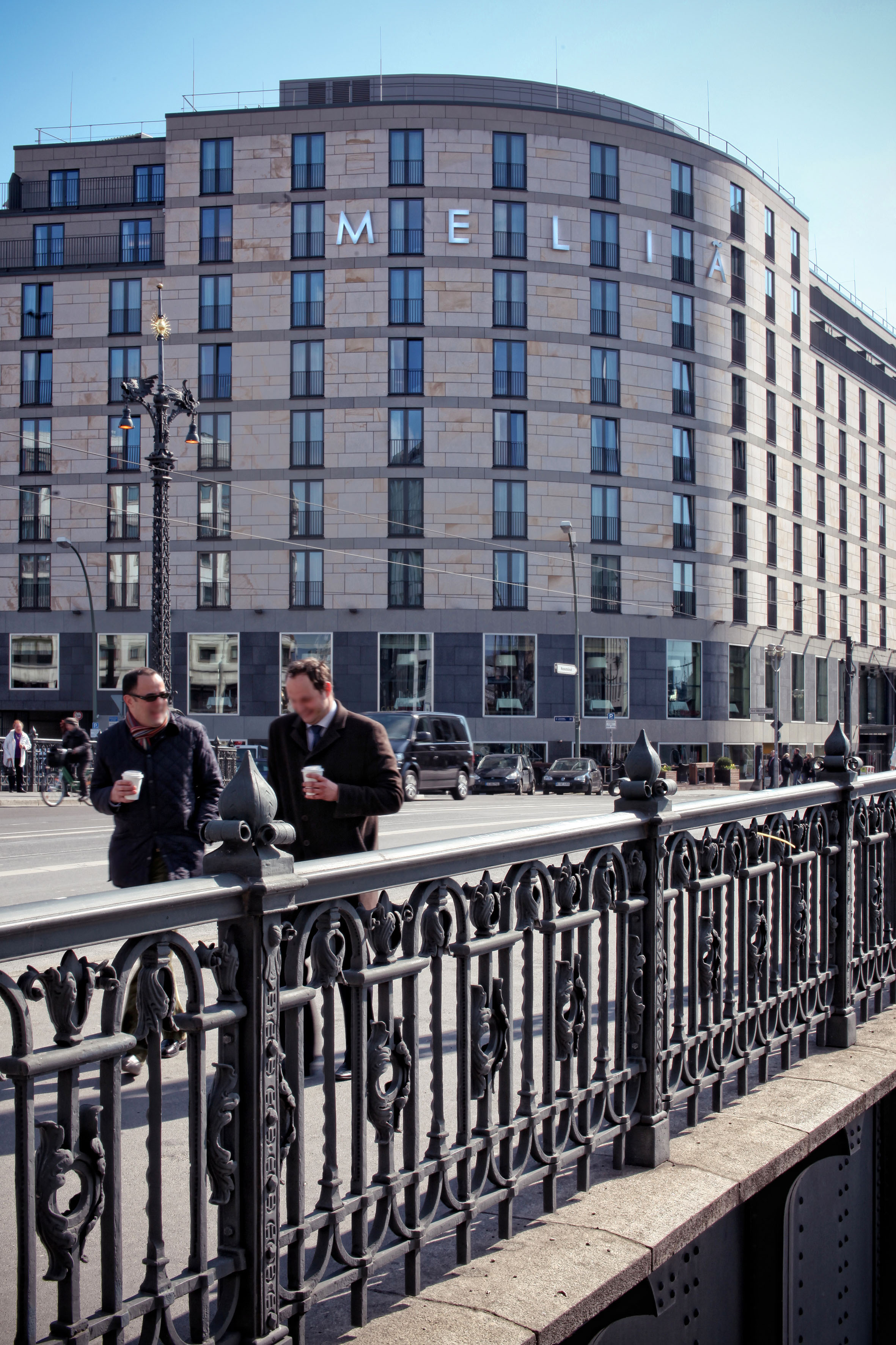 Urban street with Melia Hotel, two men, and ornate black railing.