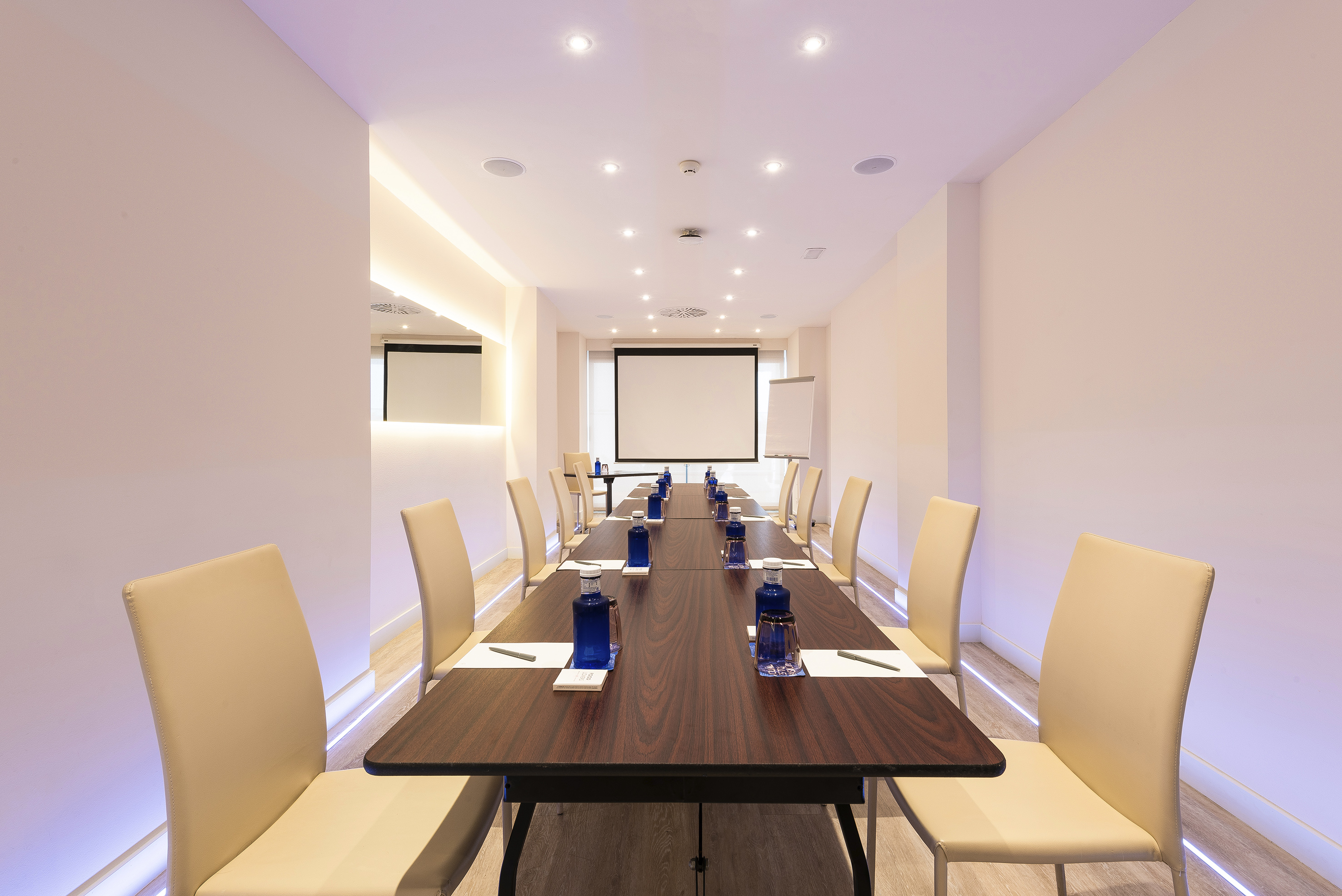 Modern conference room with large table, projector screen, and clean setup.