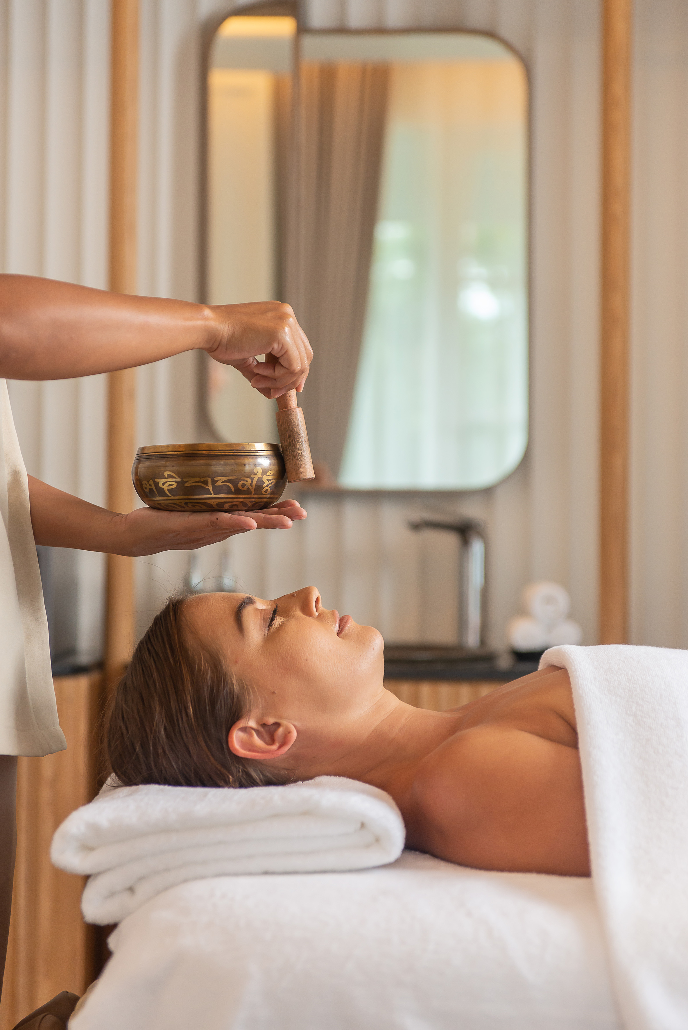 Relaxing woman receives singing bowl sound therapy in a spa setting.