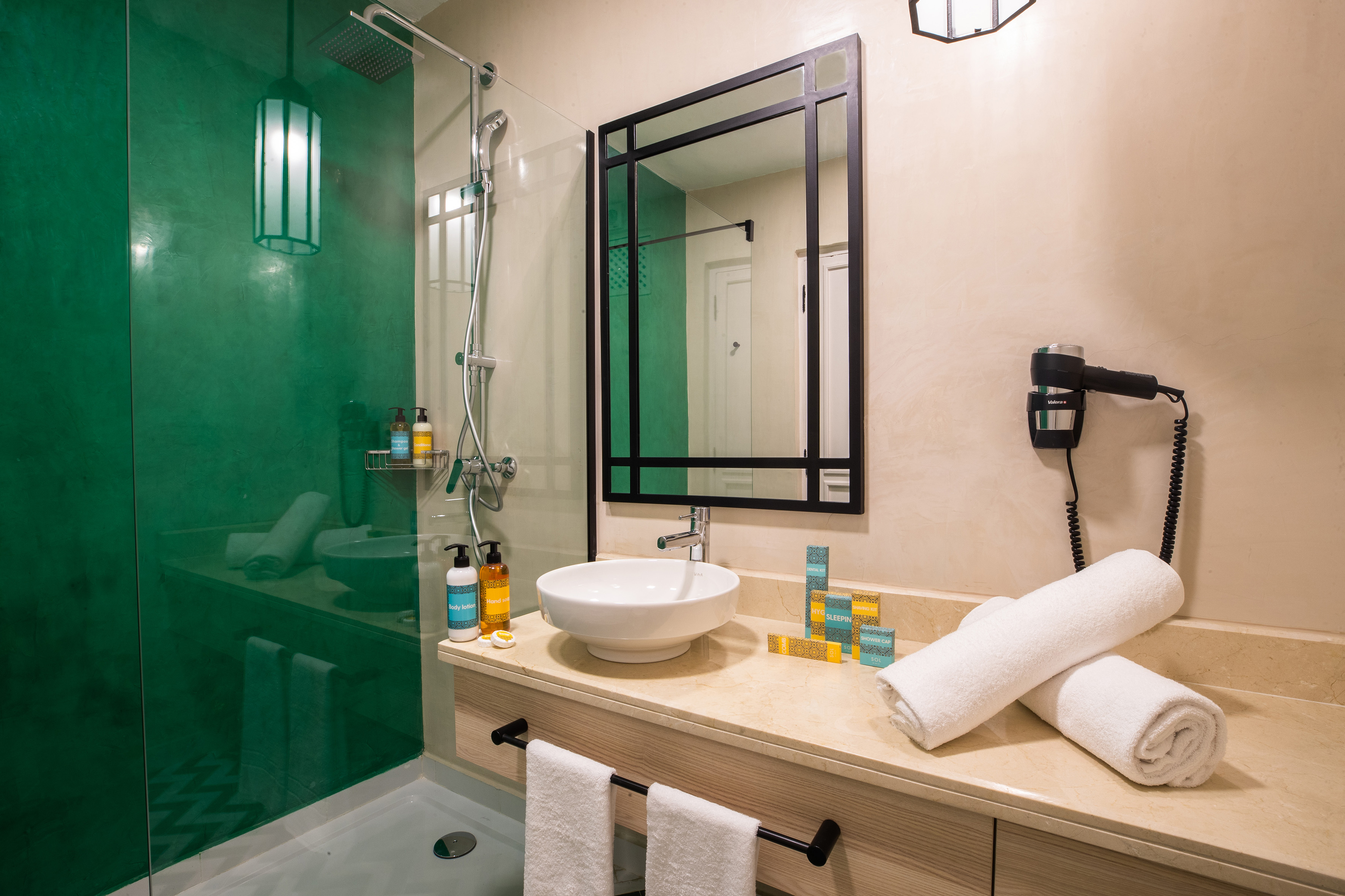 Modern bathroom with green shower, vessel sink, black mirror, and hotel amenities.