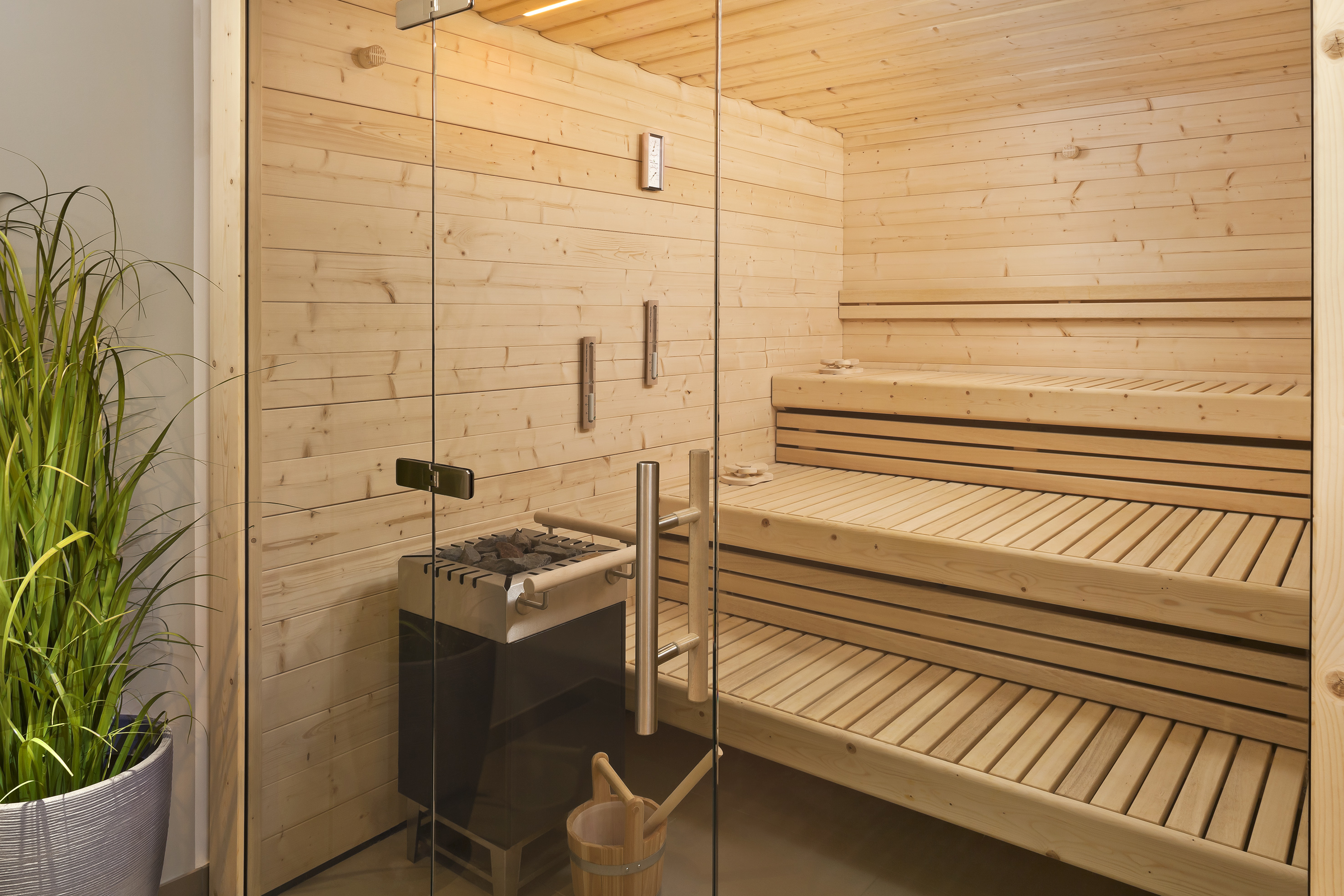 Modern wooden sauna with glass door, electric heater, and multi-tiered benches.