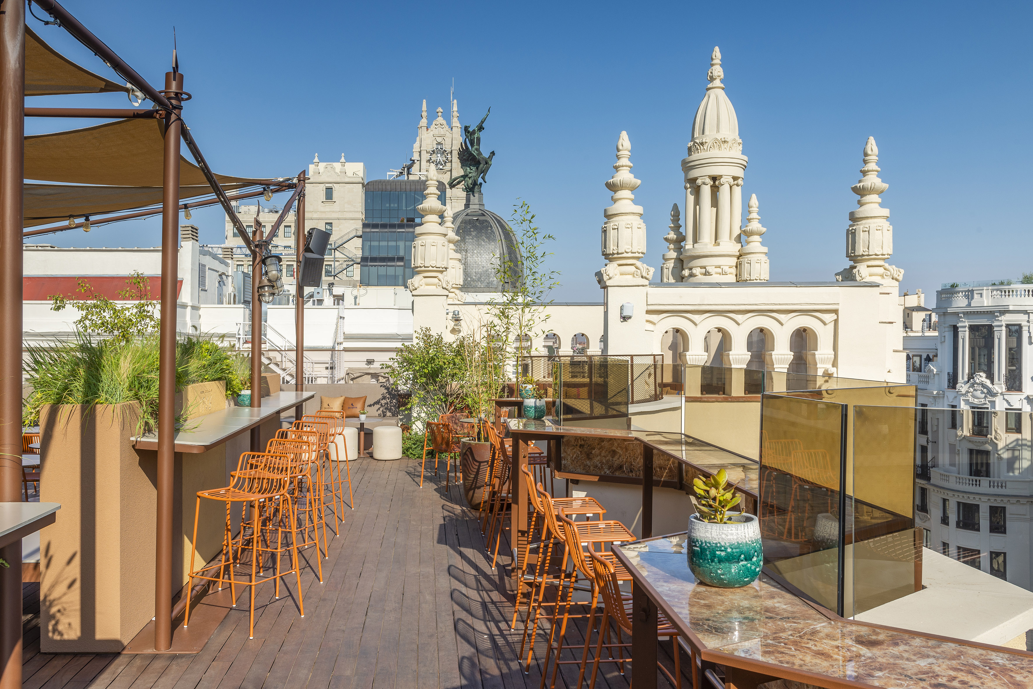 Rooftop terrace bar with orange stools, plants, and historic Madrid city skyline.