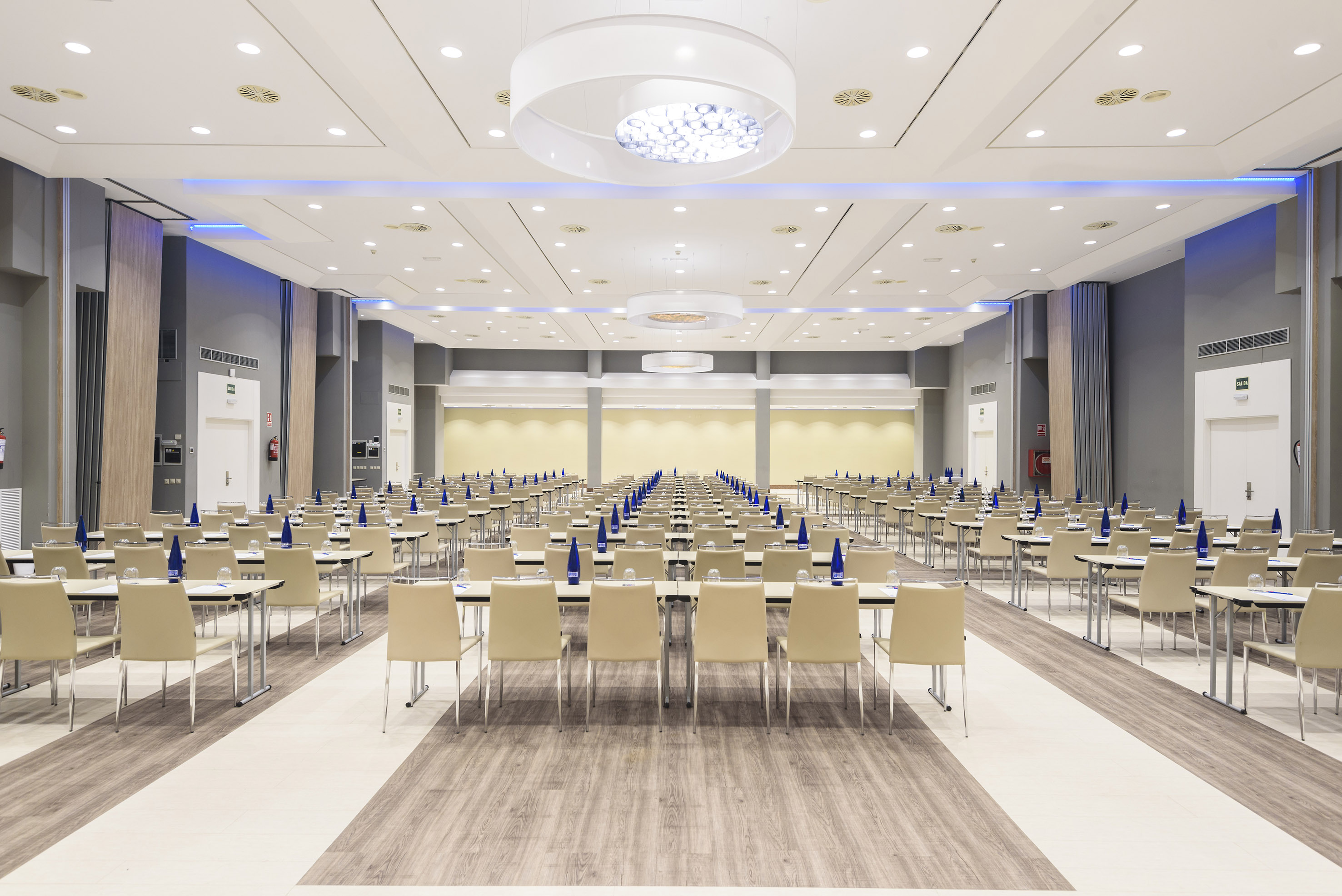 Modern empty conference room with rows of tables, chairs, and bright ceiling lights.