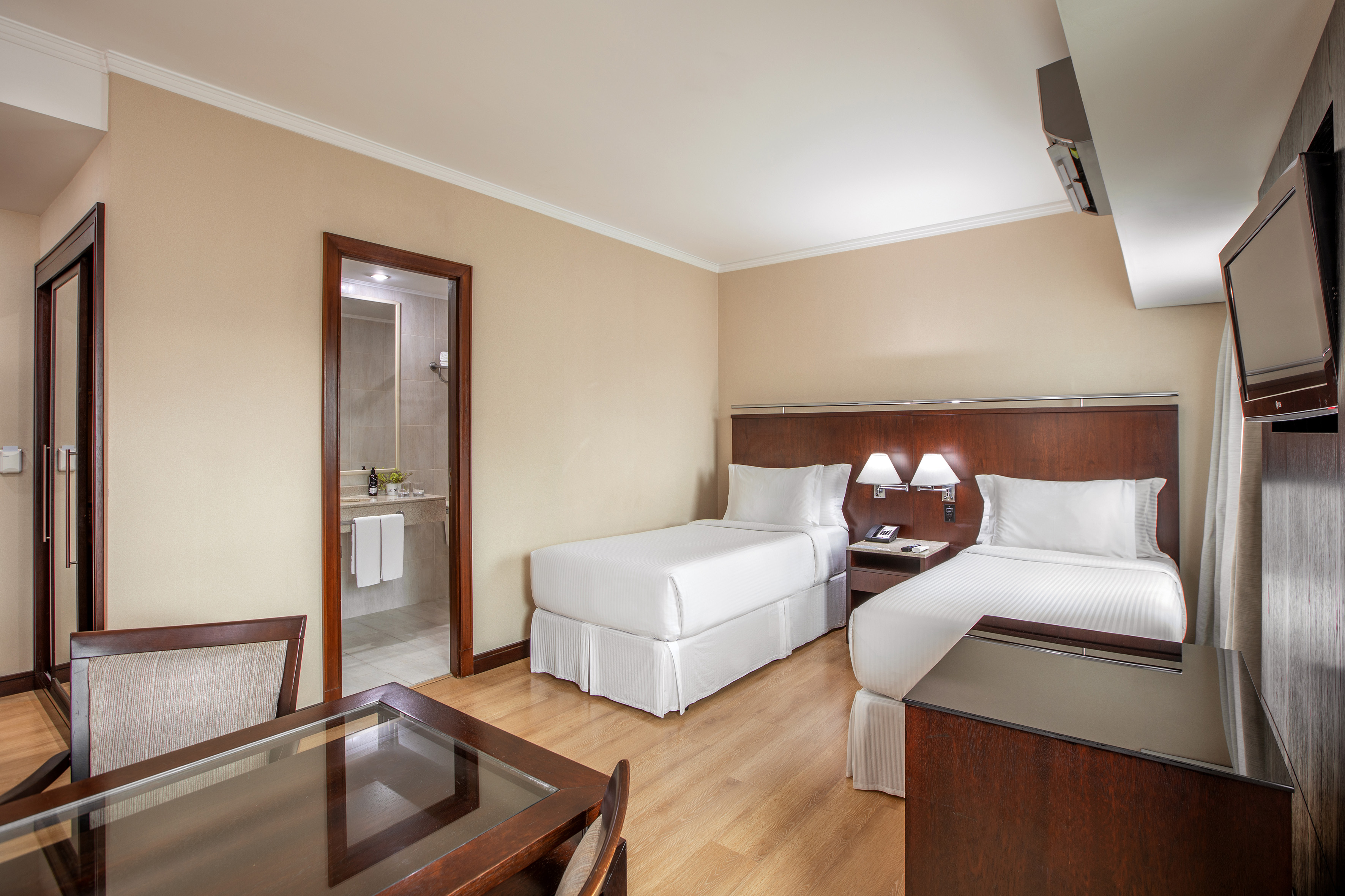 Comfortable hotel room with two twin beds, wooden furnishings, and open bathroom.
