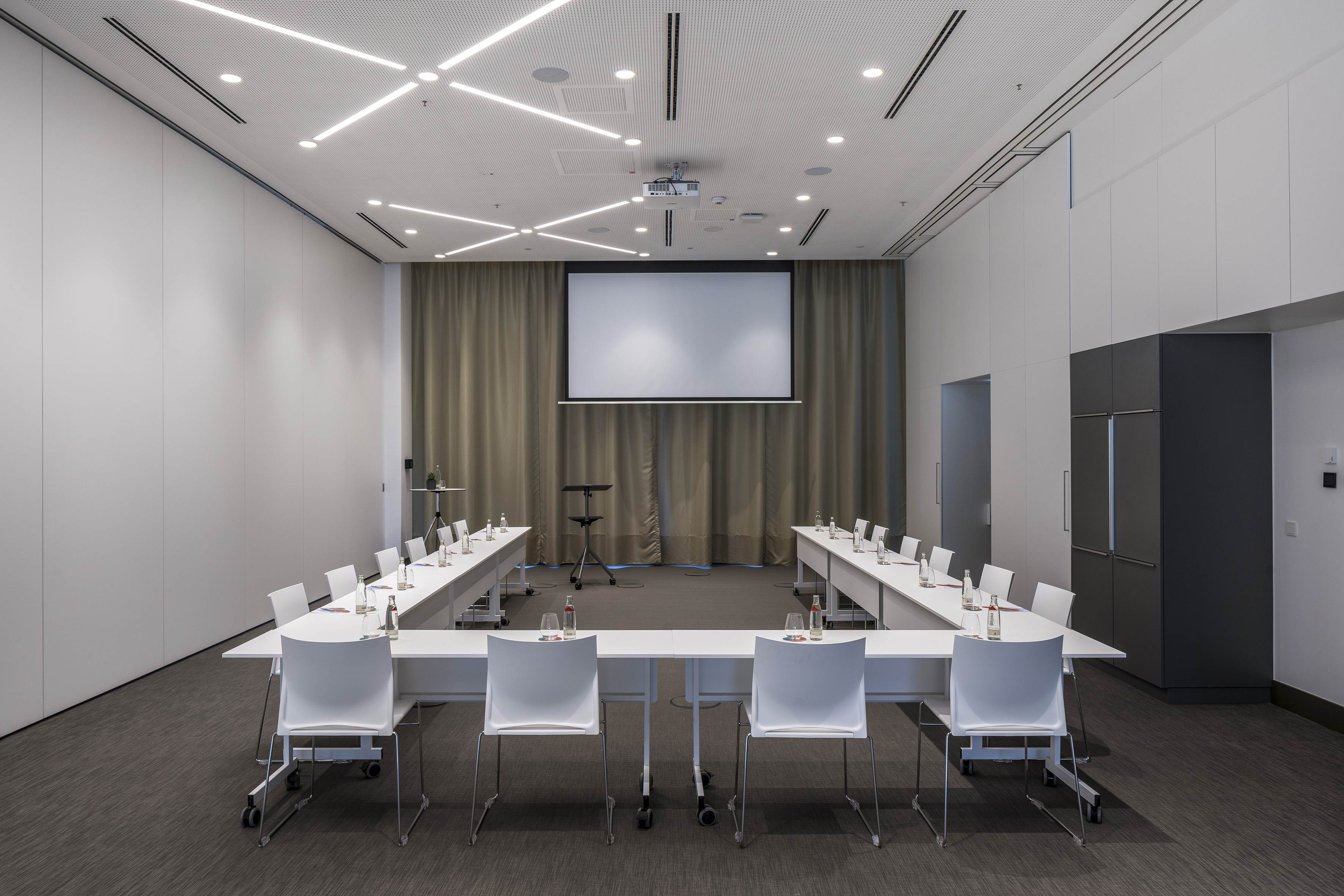 Modern U-shaped conference room with white chairs and projector screen.