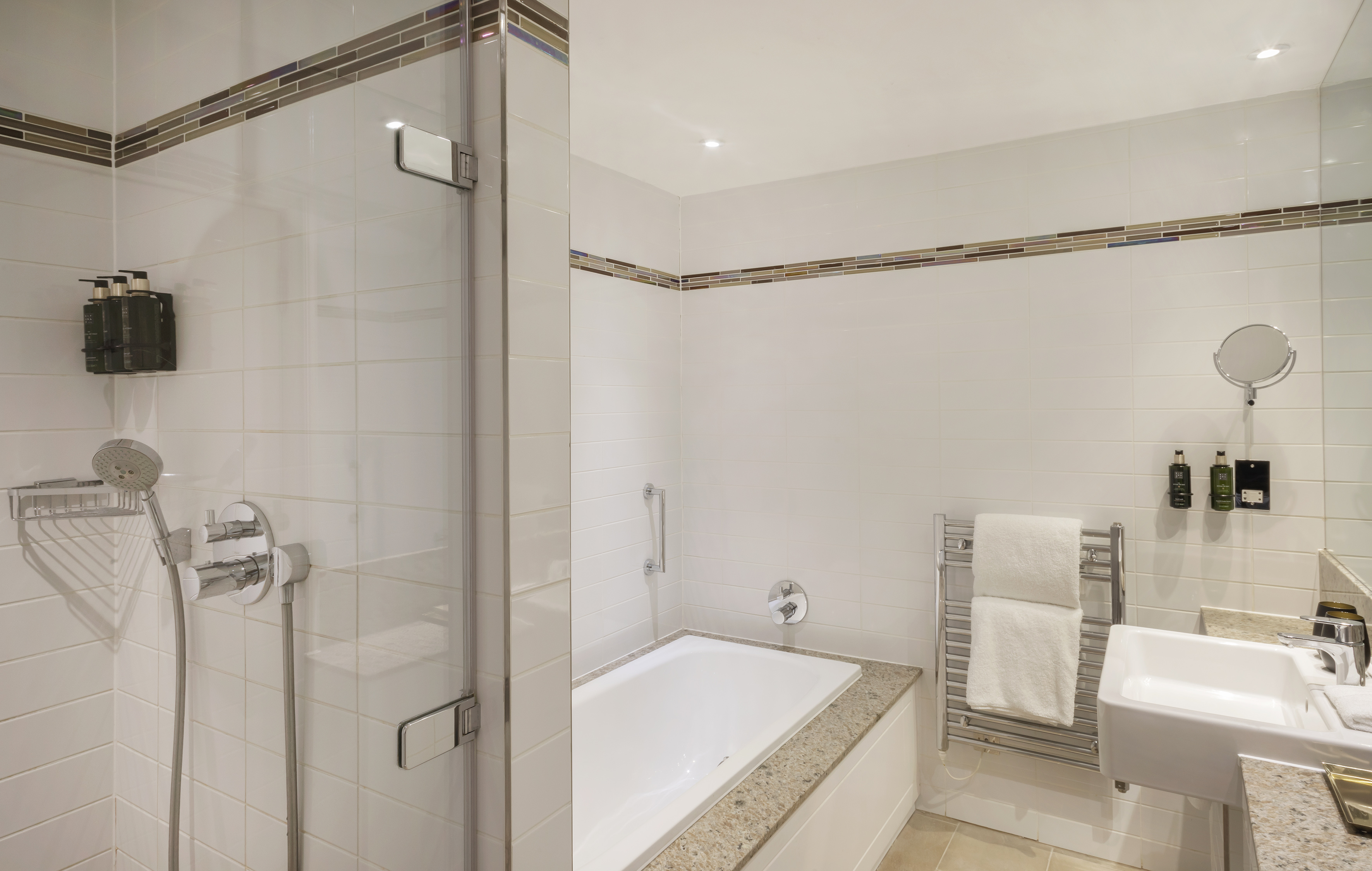 Modern tiled bathroom with glass shower, bathtub, sink, and towel warmer.