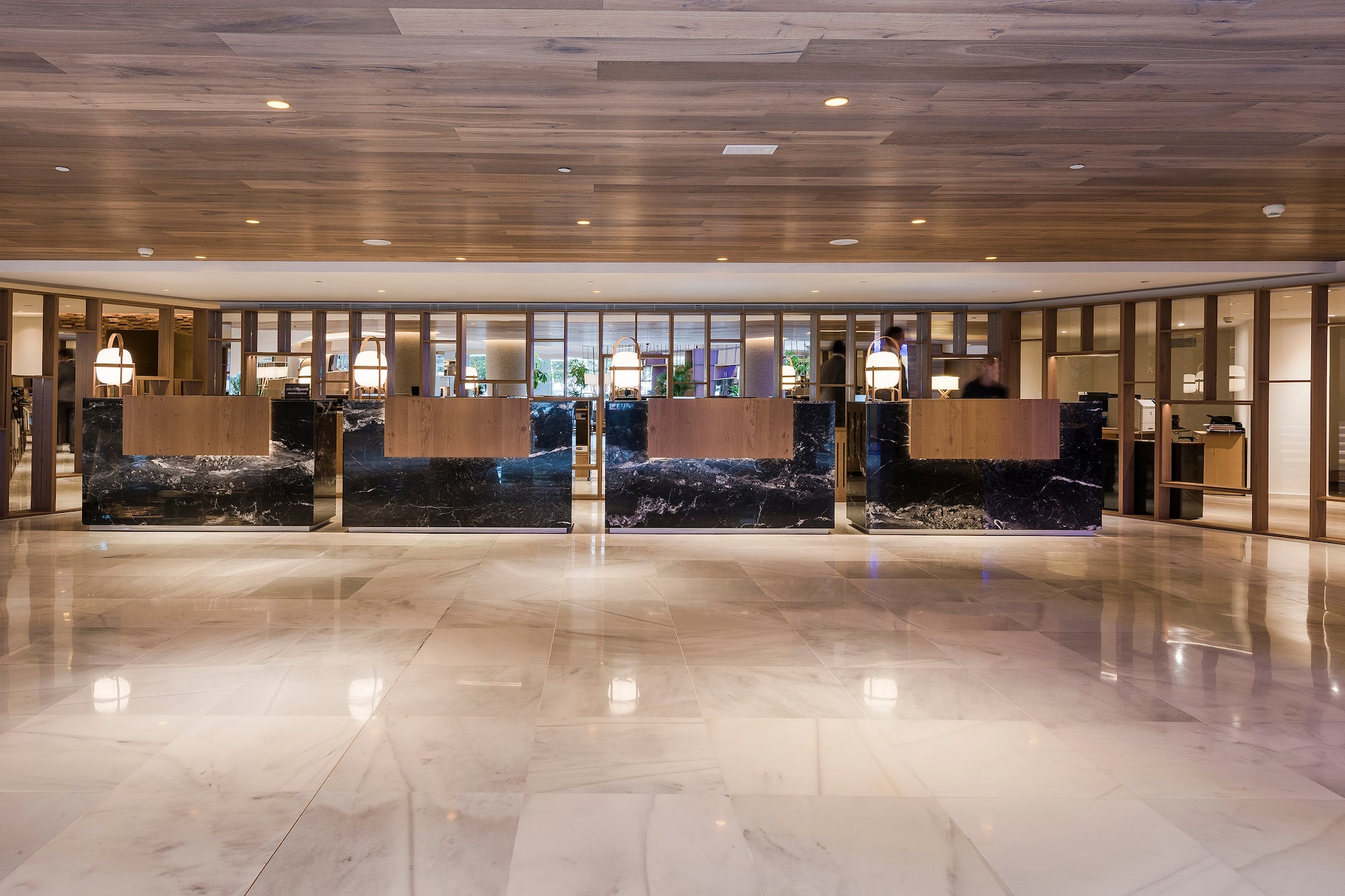 Modern hotel reception lobby with four black marble and wood desks.