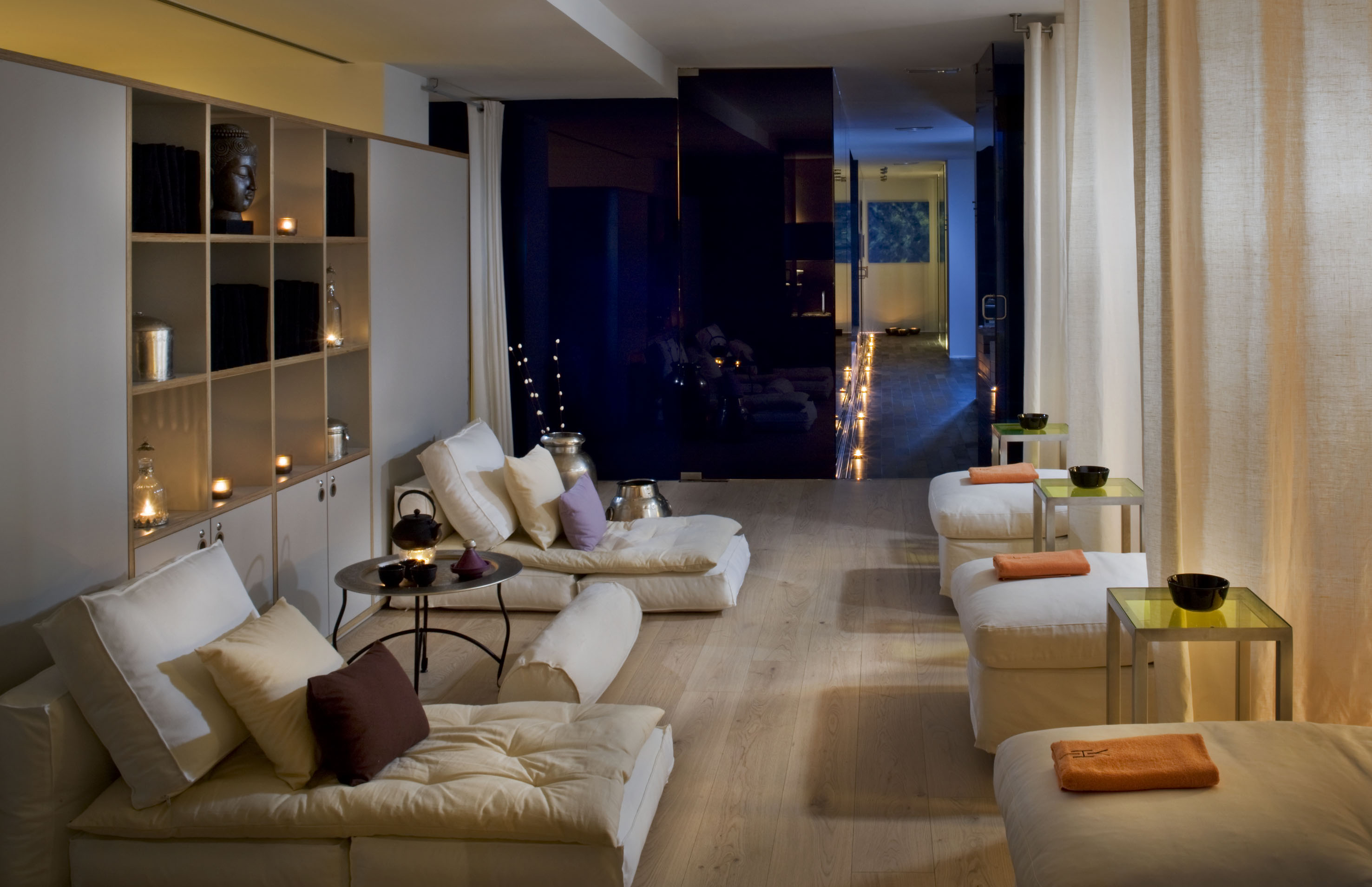 Relaxing spa lounge with soft daybeds, candlelit shelves, and warm lighting.