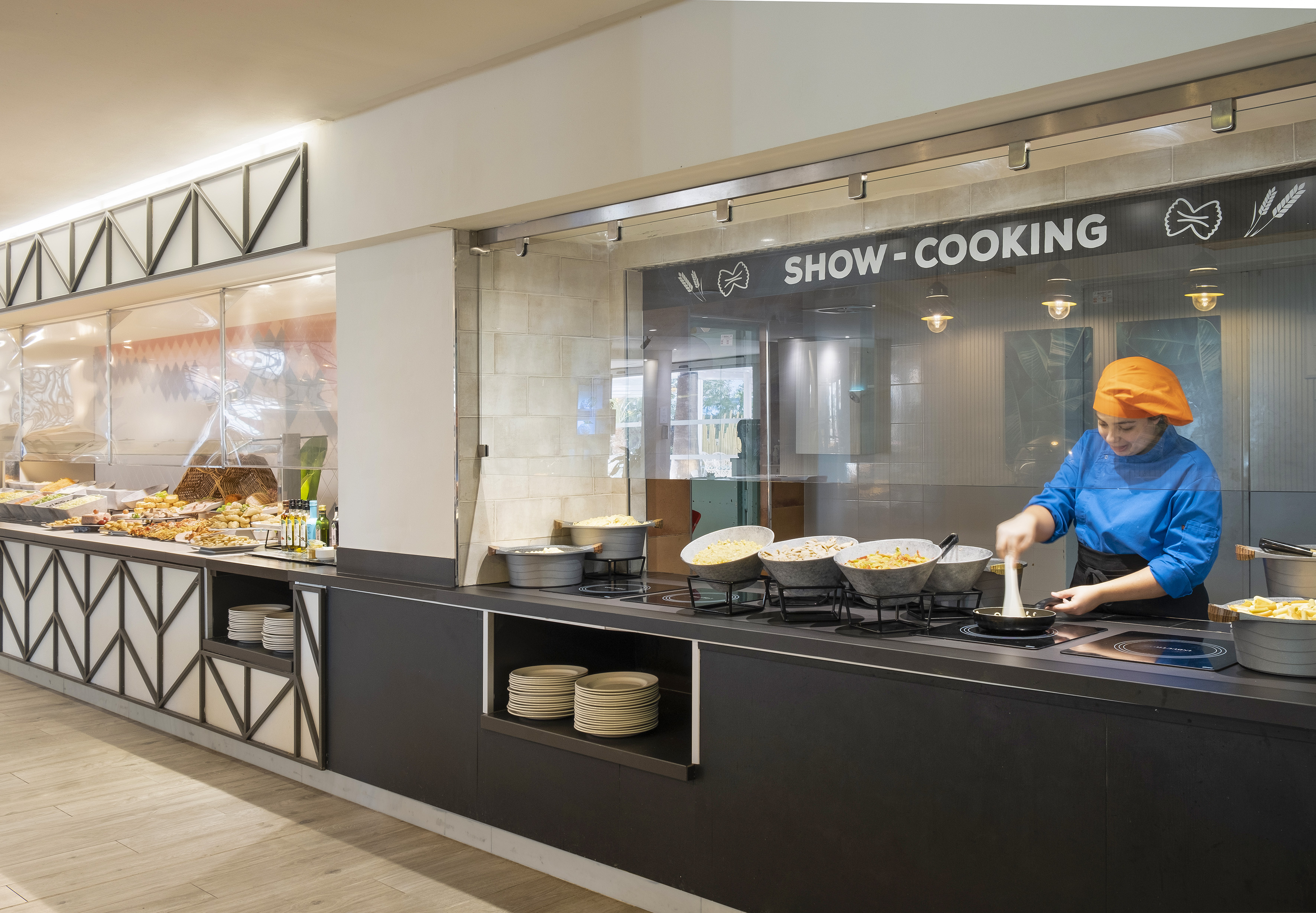 Chef cooking at a show-cooking buffet station in a modern hotel restaurant.