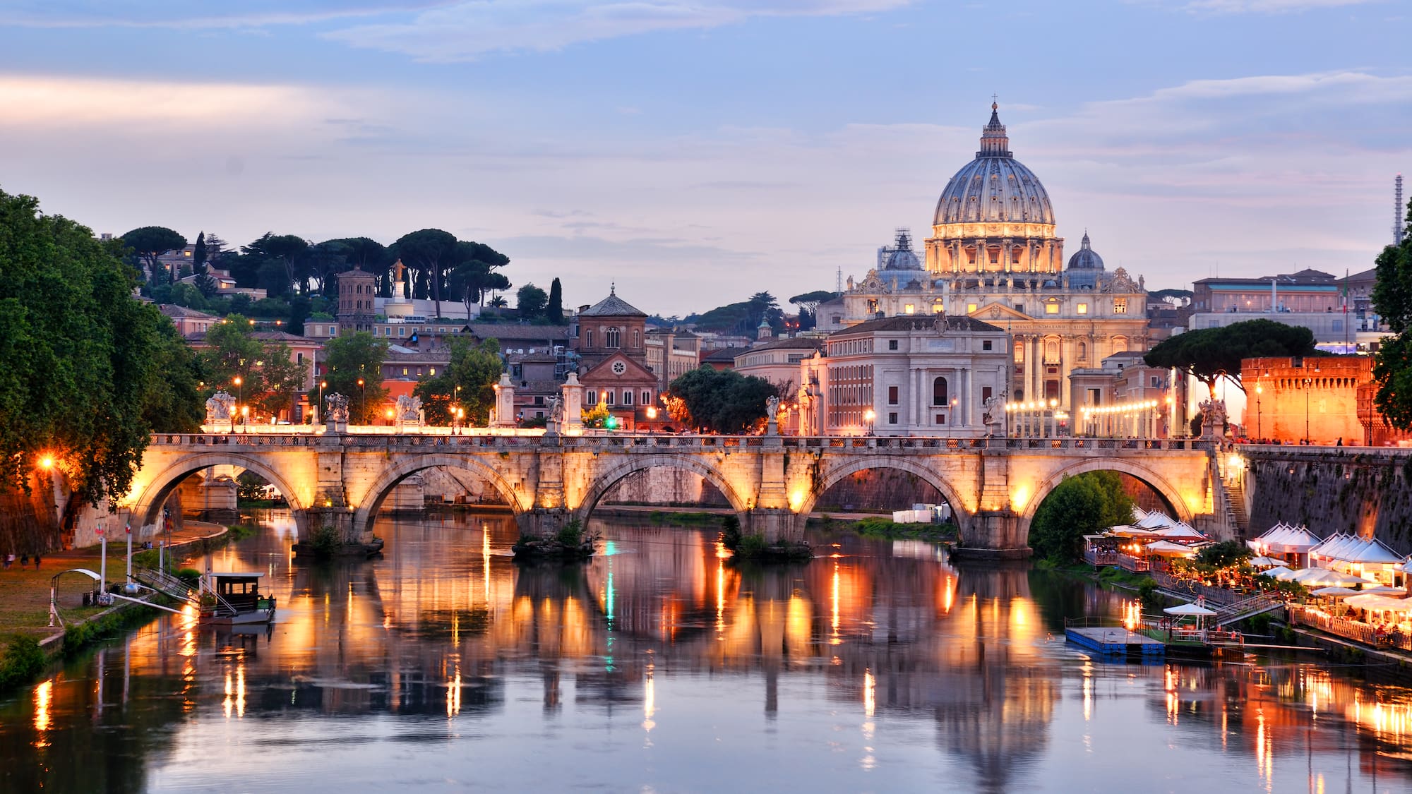 a bridge over a river with a dome and buildings in the background