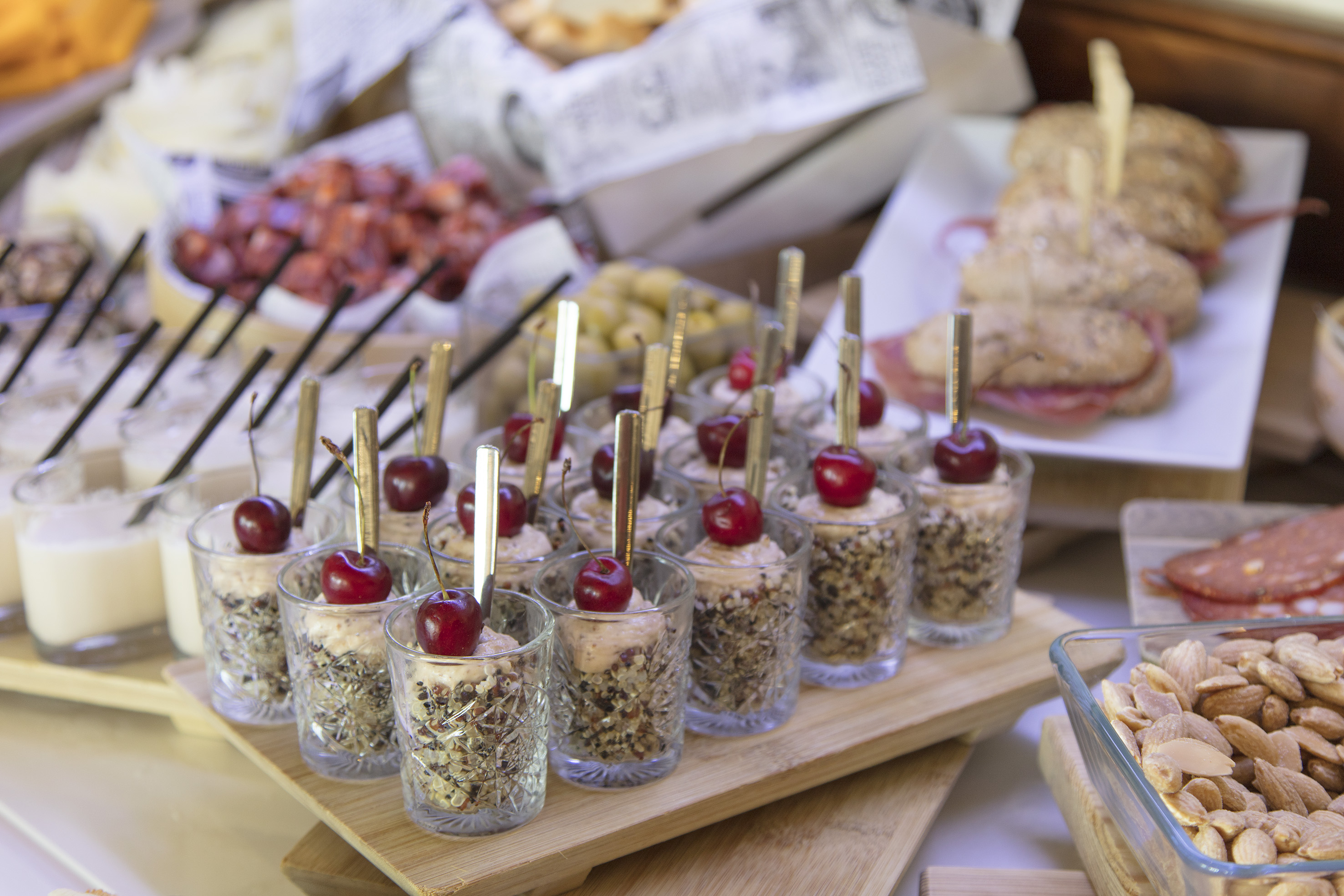 Buffet with cherry parfaits, mini sandwiches, almonds, olives, and charcuterie.