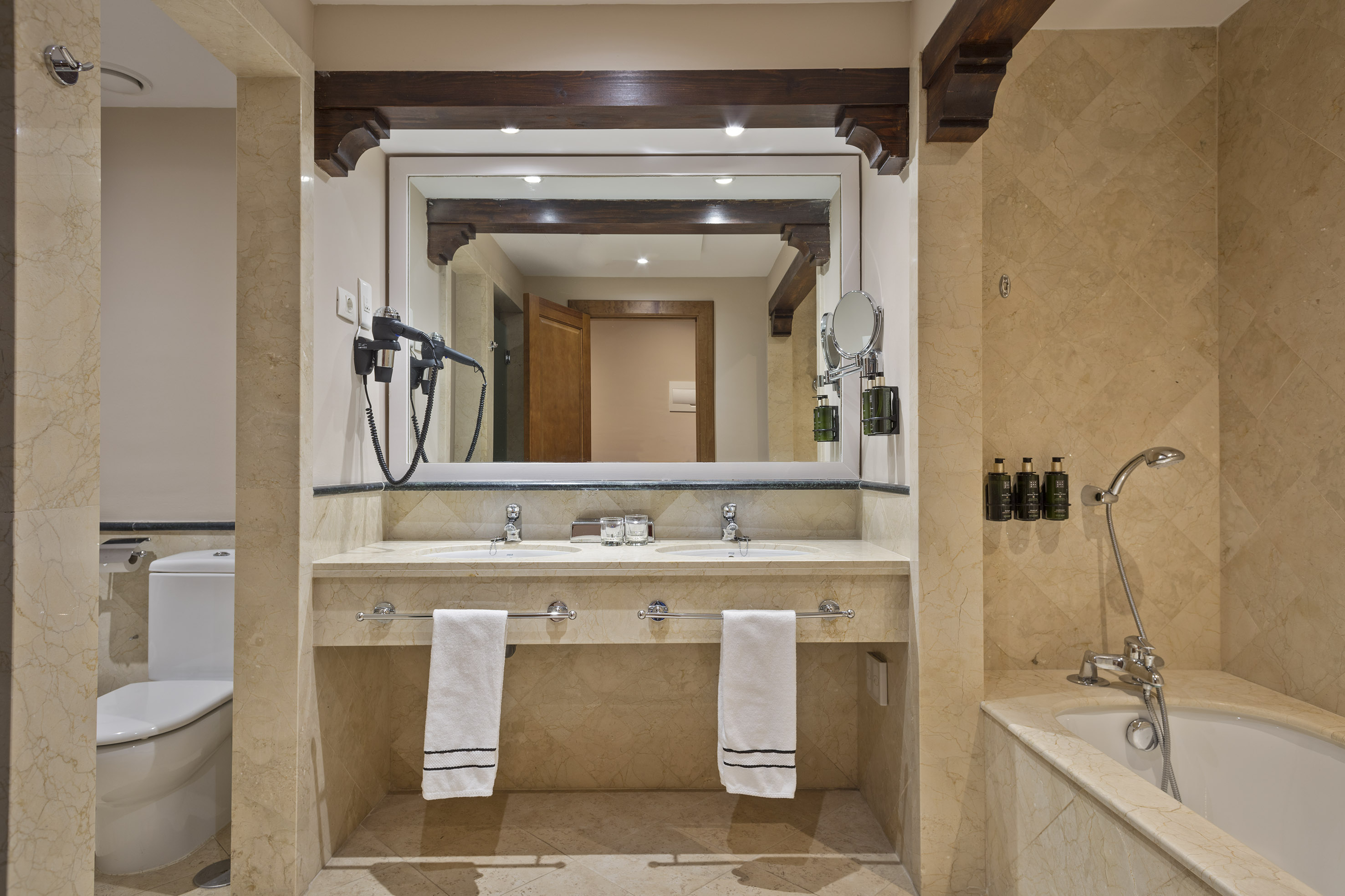 Marble hotel bathroom with double vanity, large mirror, toilet, and bathtub.
