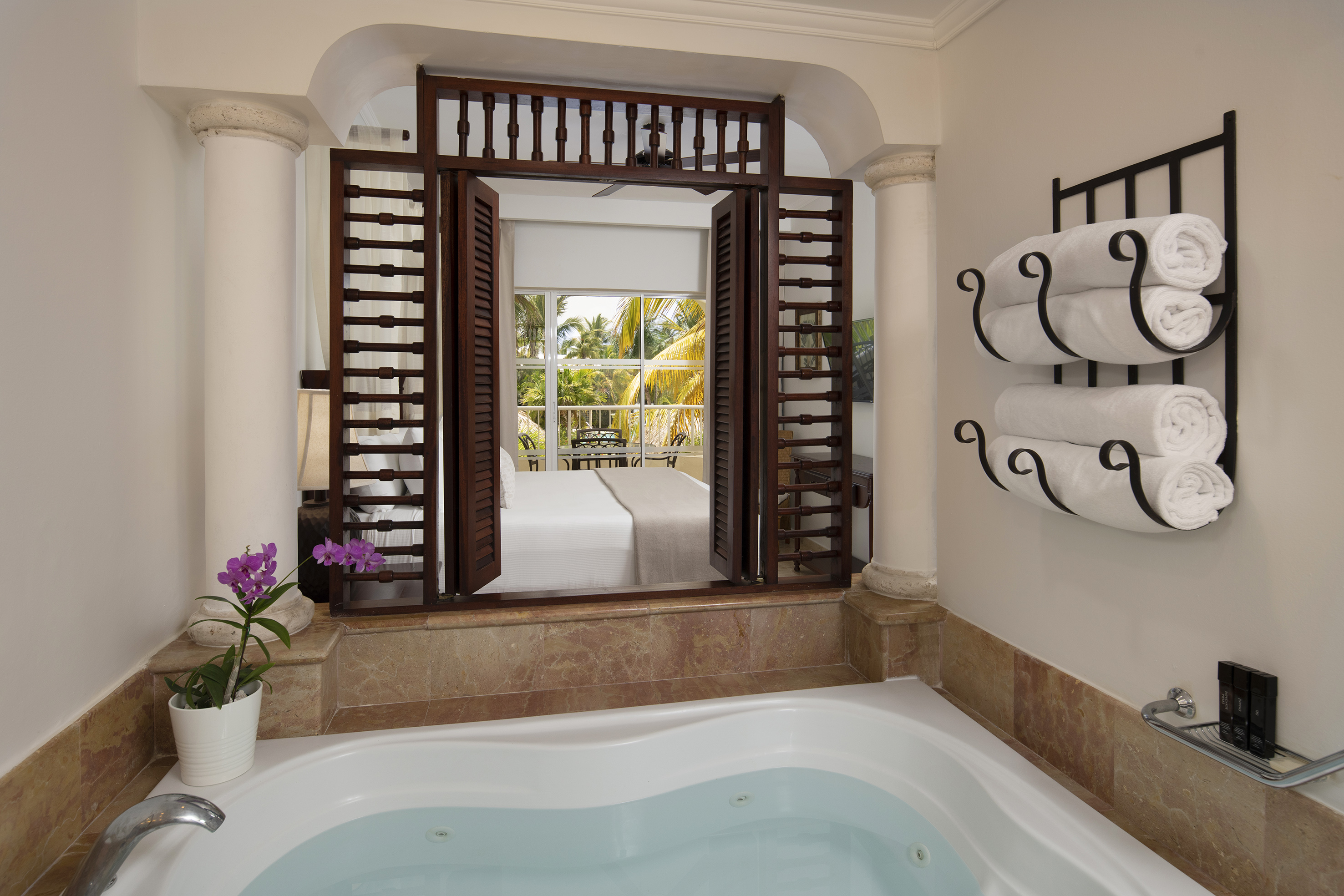Tropical hotel suite: Jacuzzi tub, open shutters to bedroom & balcony.