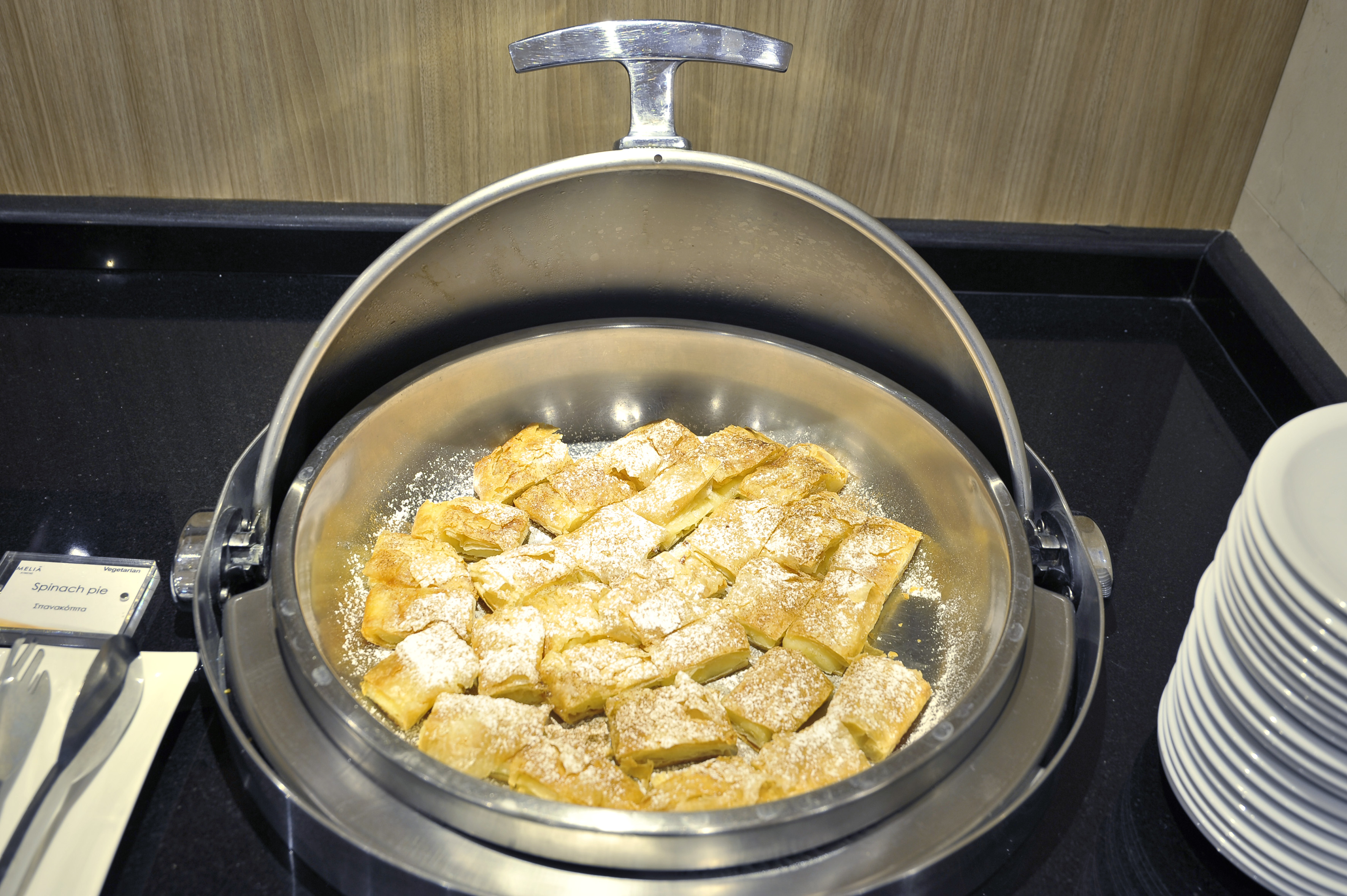Golden spinach pie squares with powdered sugar in a buffet chafing dish.