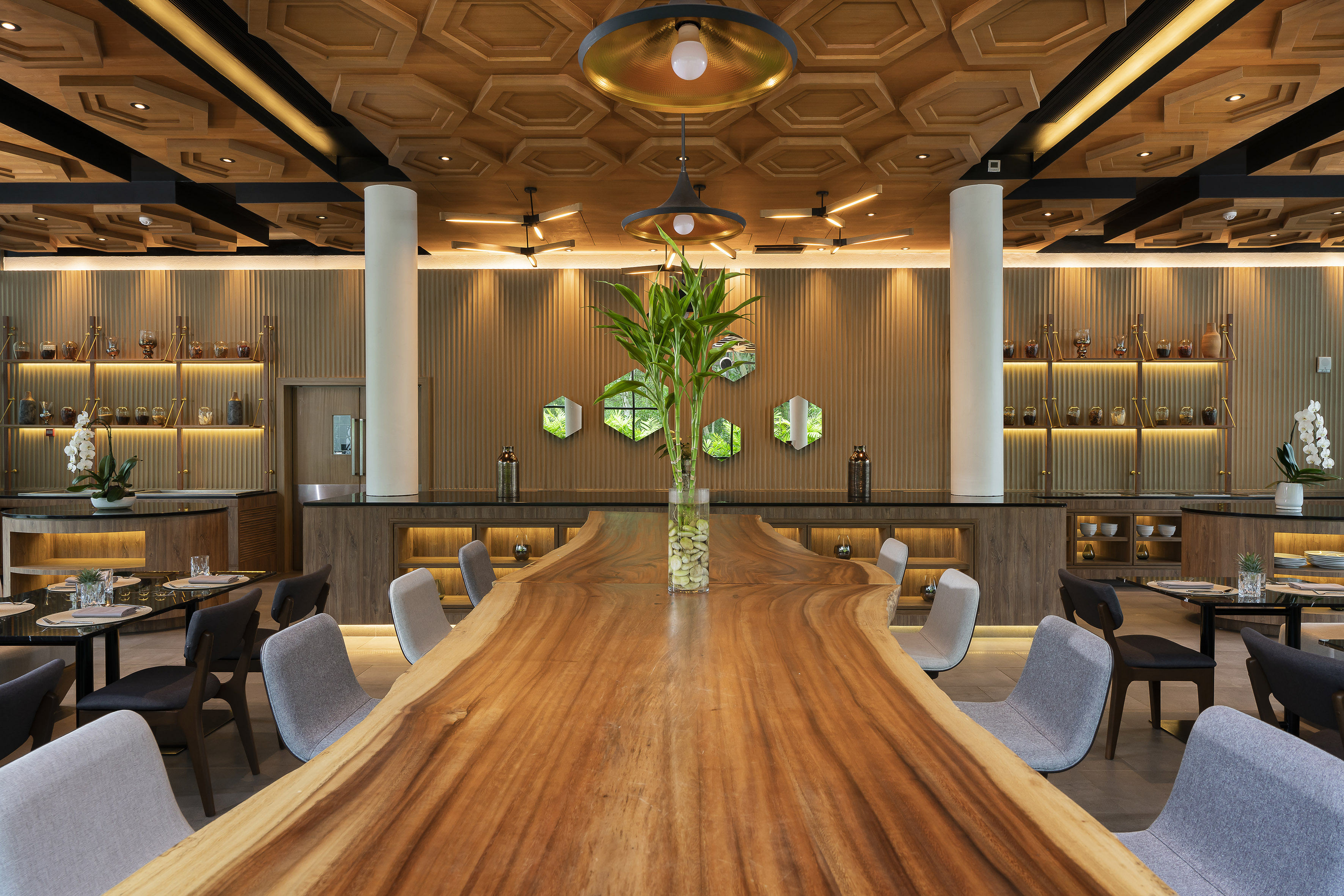 Modern restaurant with live-edge wood table, hexagonal ceiling, and warm lighting.