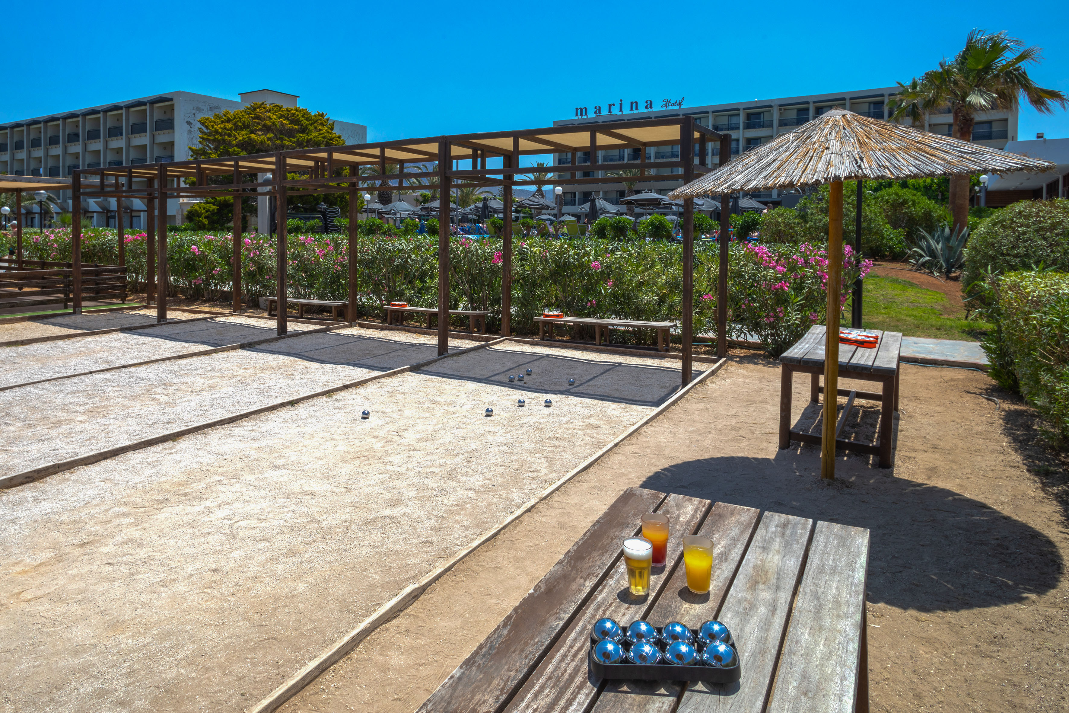 Bocce ball court at Marina Hotel with balls on sand, drinks on table, sunny.