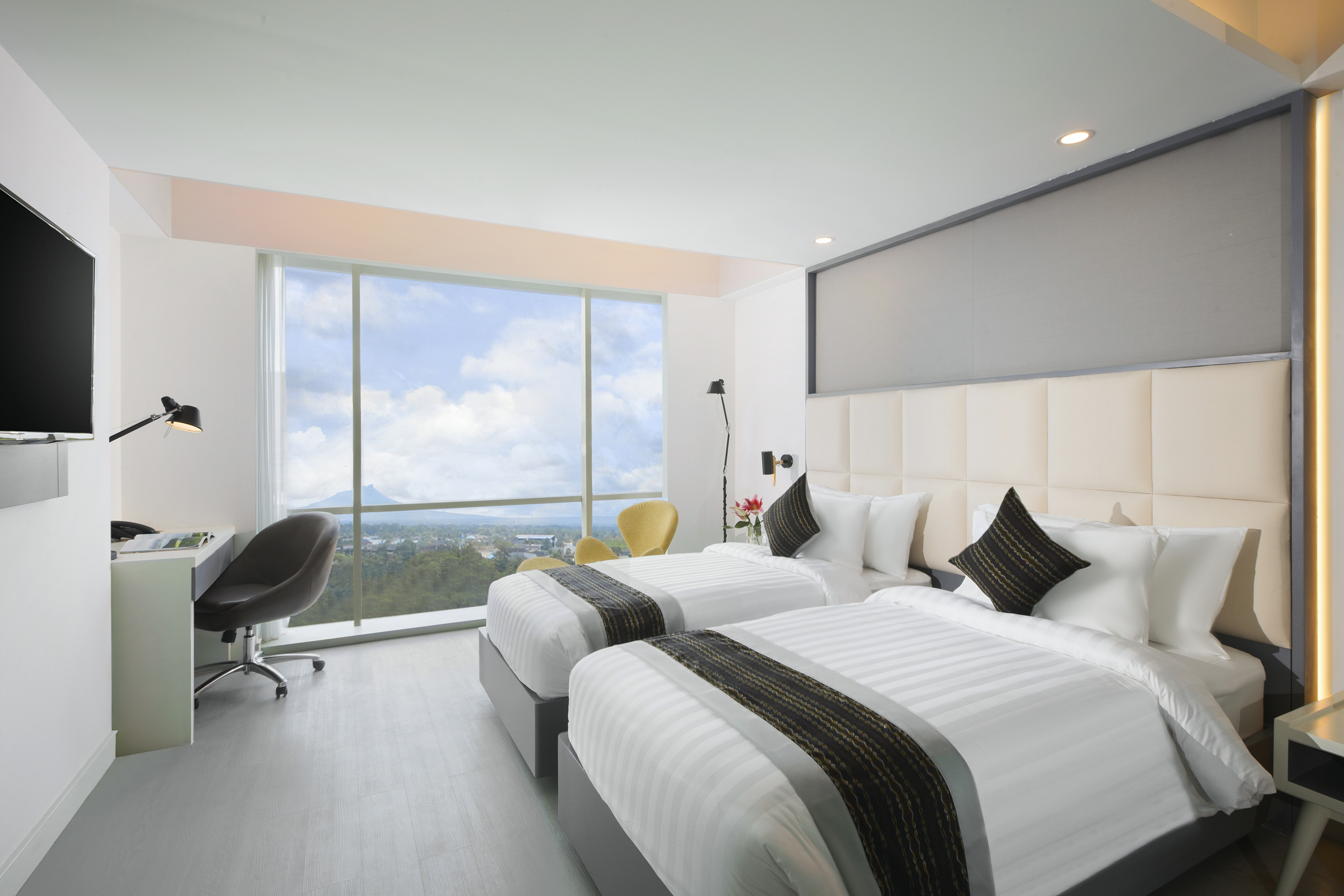 Modern twin bedroom with work desk and window offering a city and mountain view.