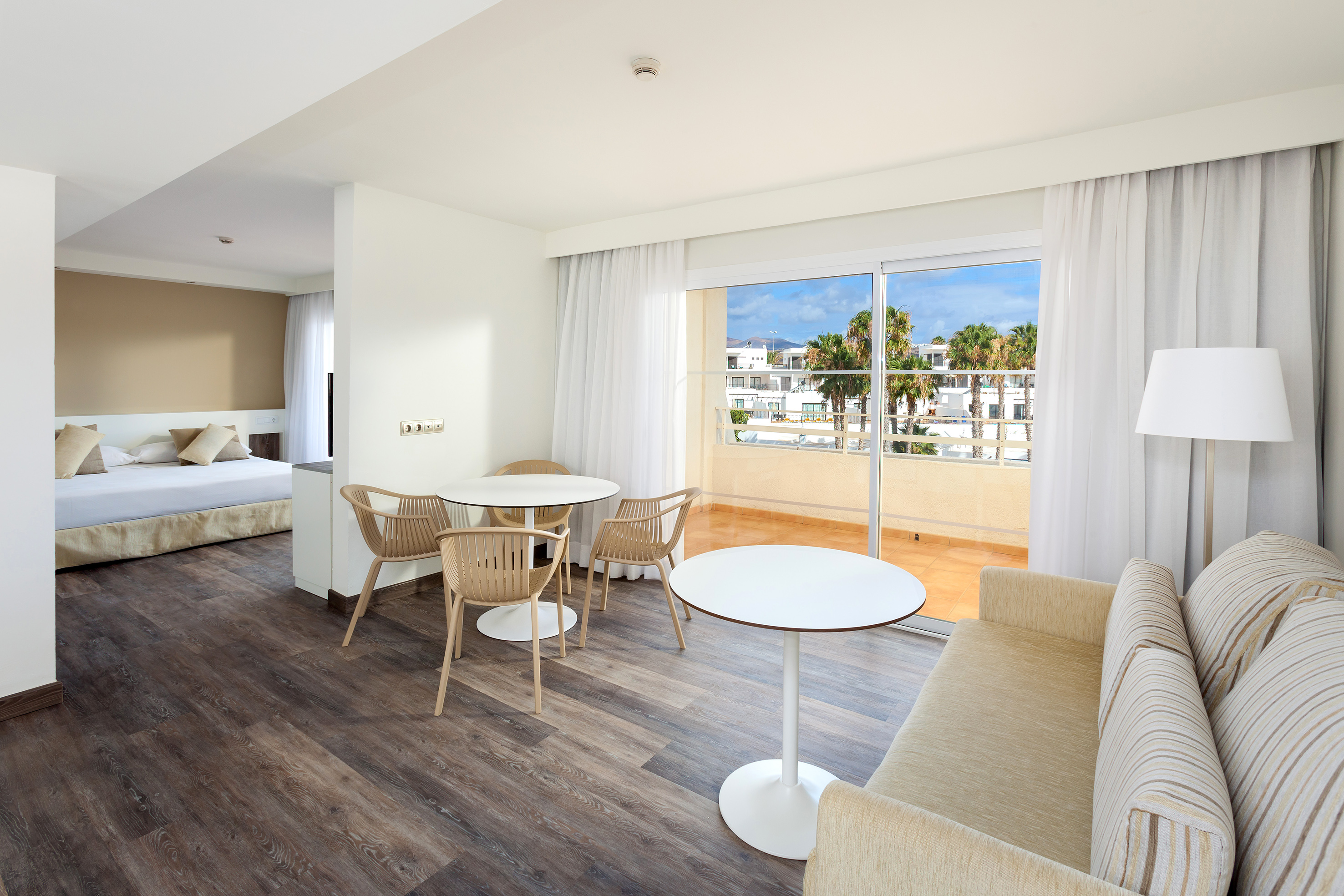 Spacious hotel suite: living area, dining table, bedroom, balcony, resort view.