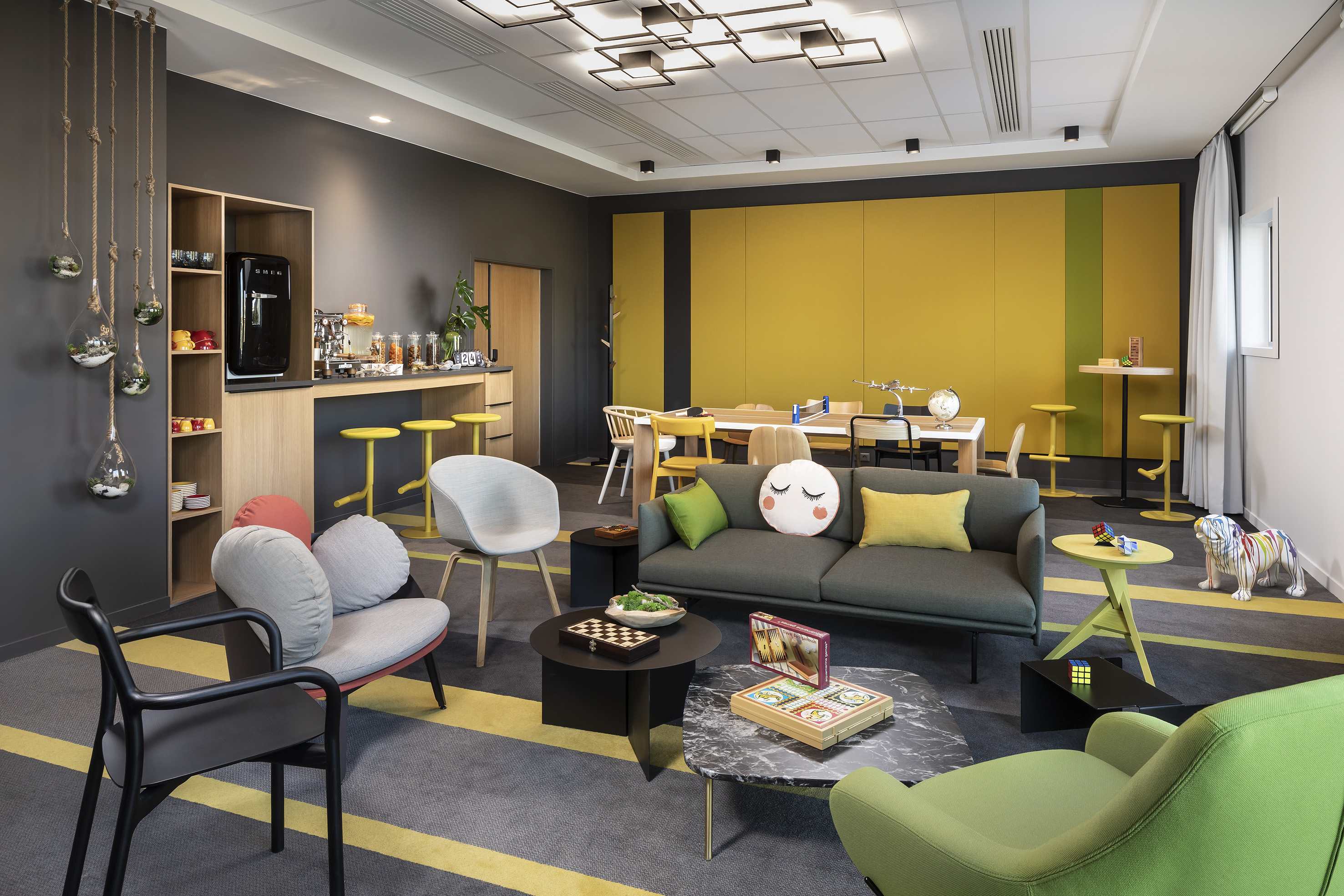 Vibrant office lounge with coffee bar, yellow accent wall, and casual seating.