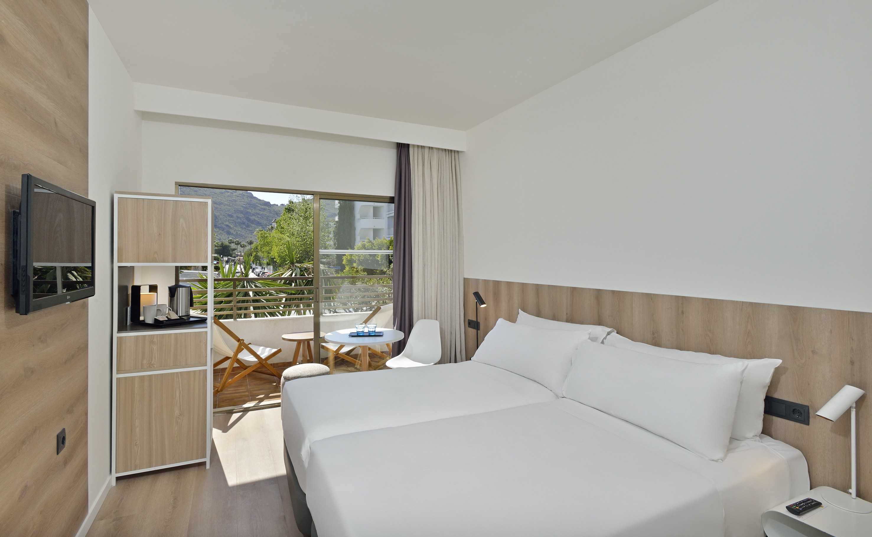 Hotel bedroom with twin beds, private balcony, and scenic mountain view.