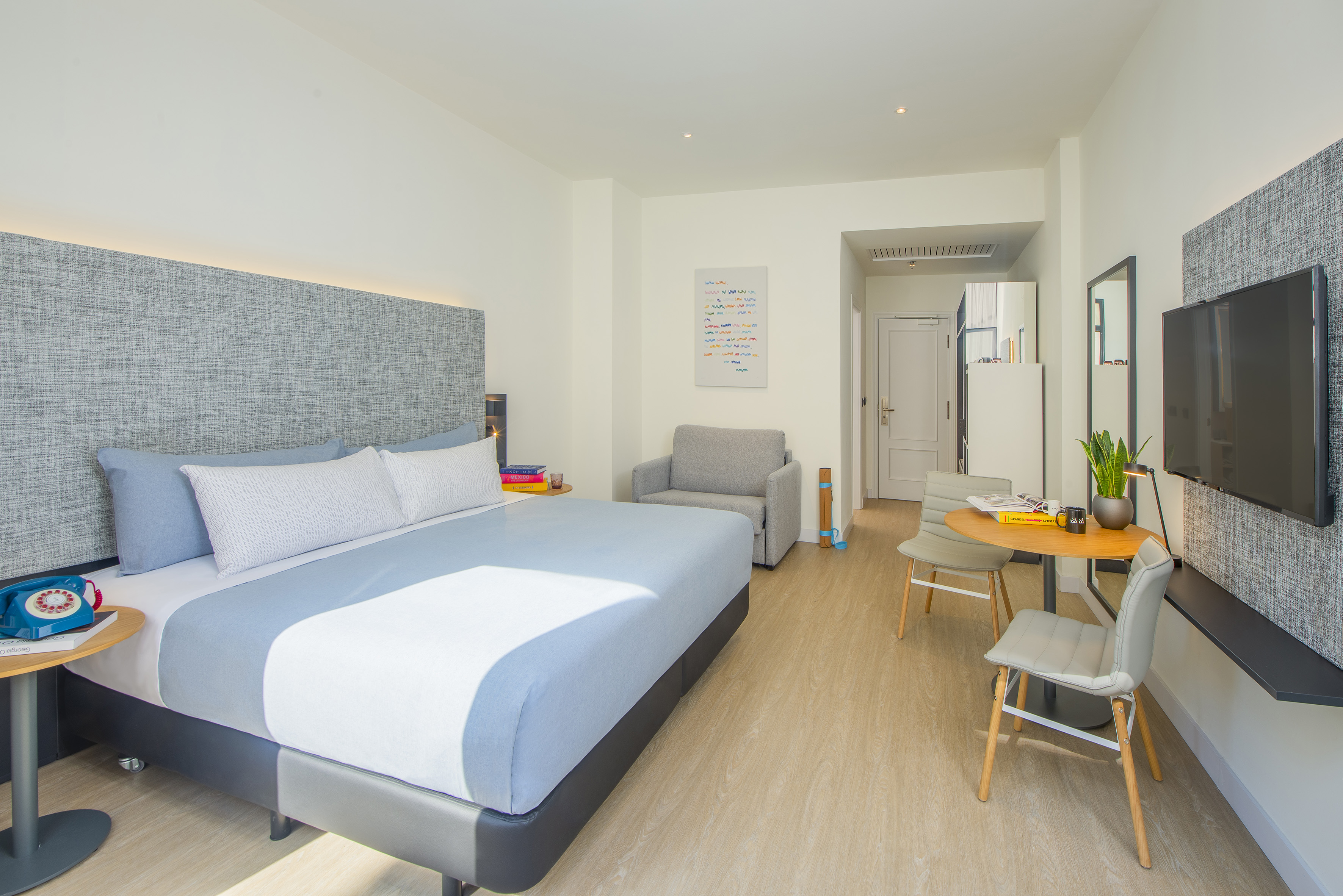 Modern hotel suite with king bed, lounge area, dining table, and TV.