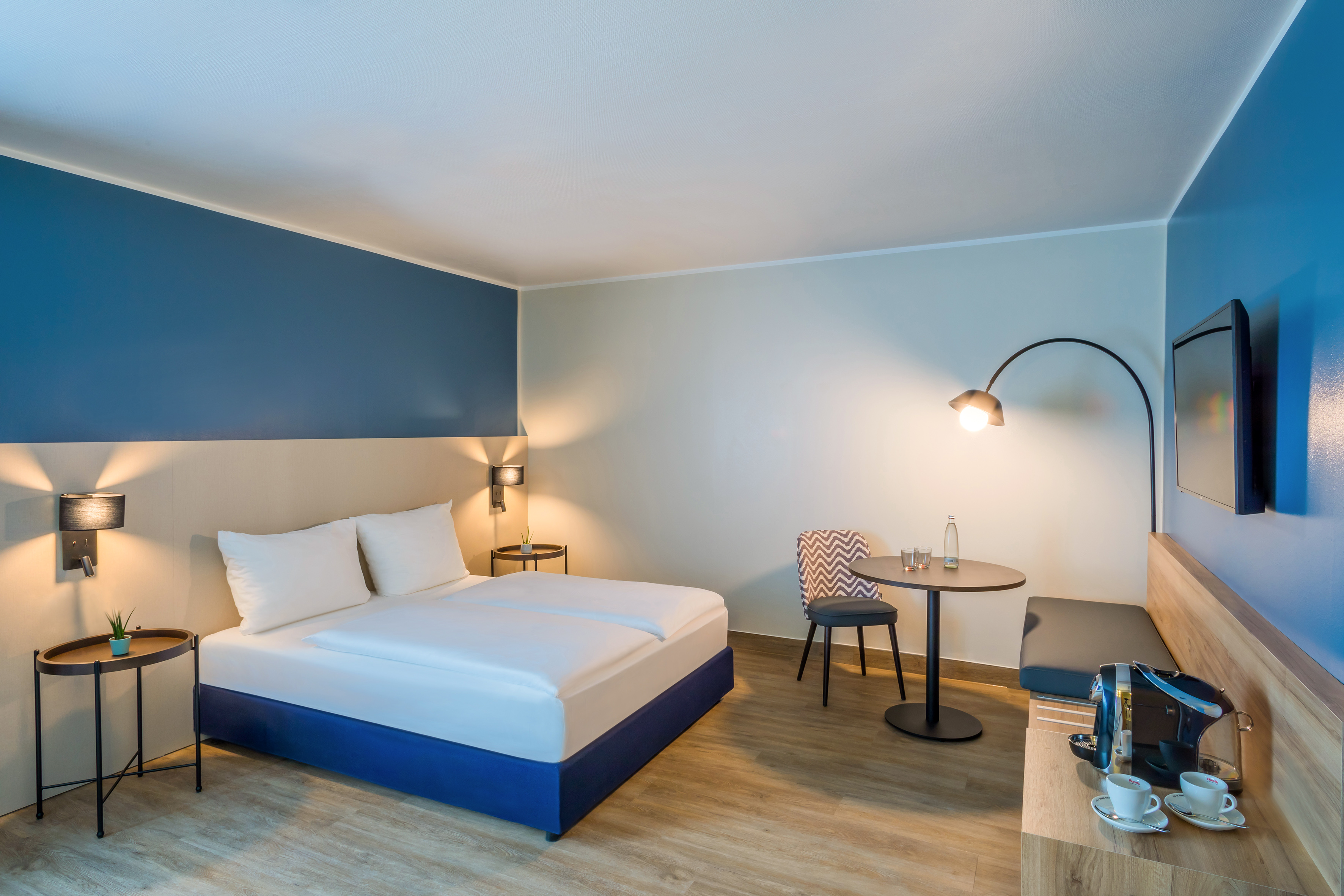 Modern hotel room with blue accent walls, comfortable bed, and coffee station.