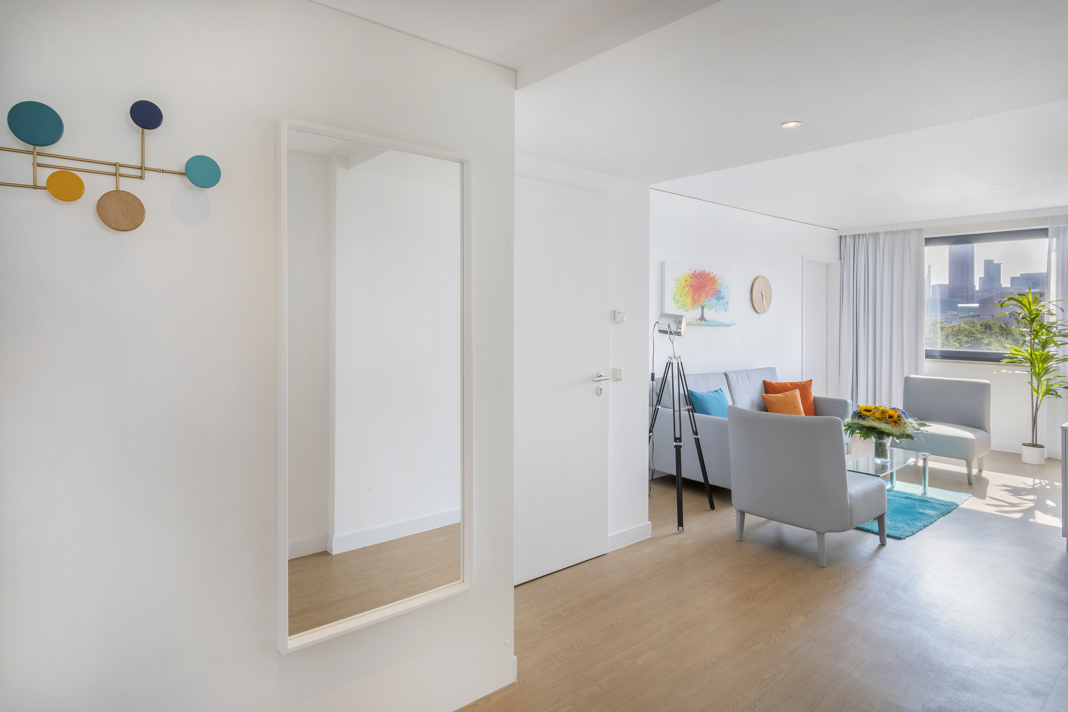 Bright modern apartment hallway and living room with mirror, sofa, and city view.