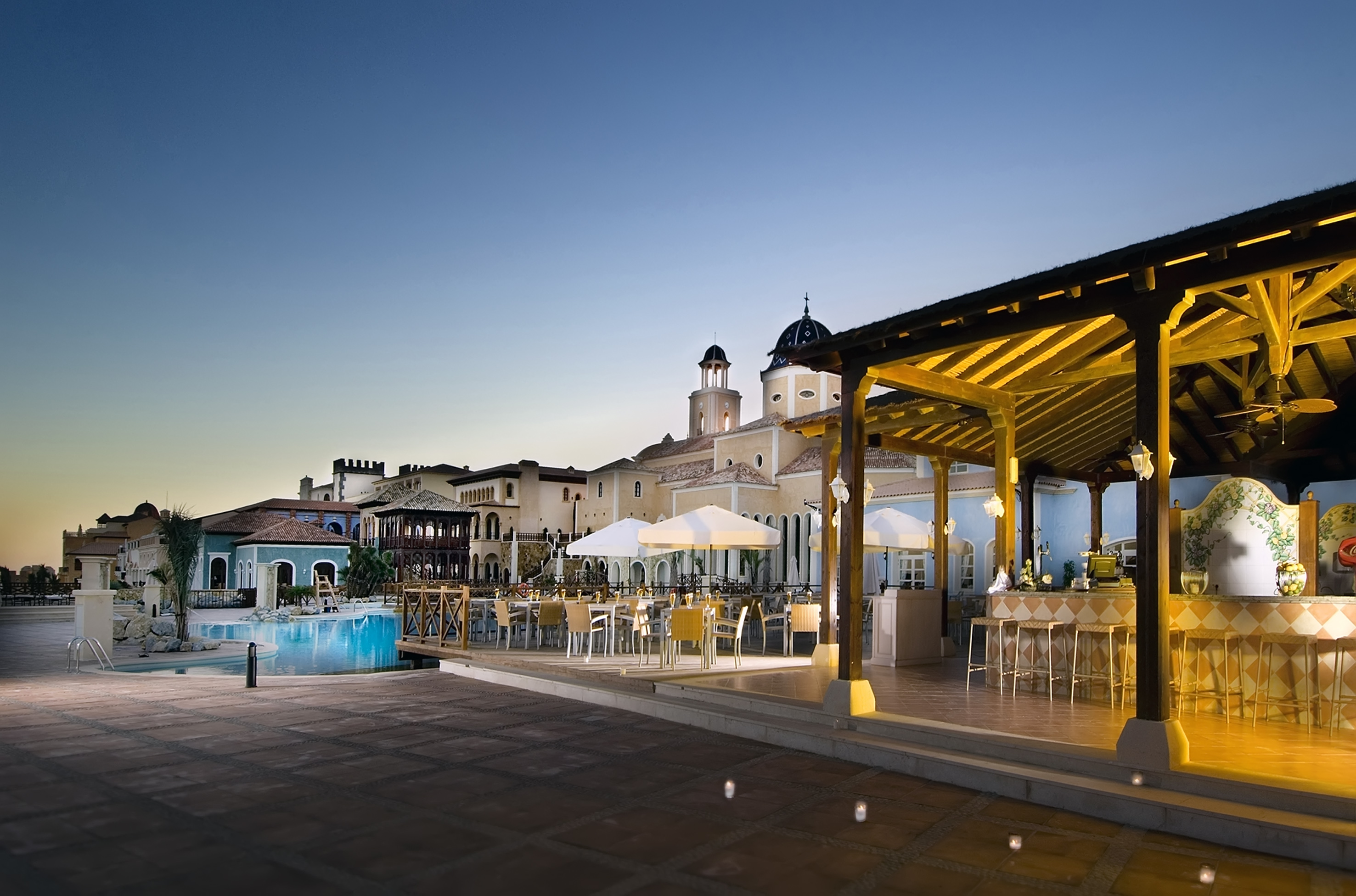 Luxury resort outdoor bar, dining, and pool area under an evening sky.