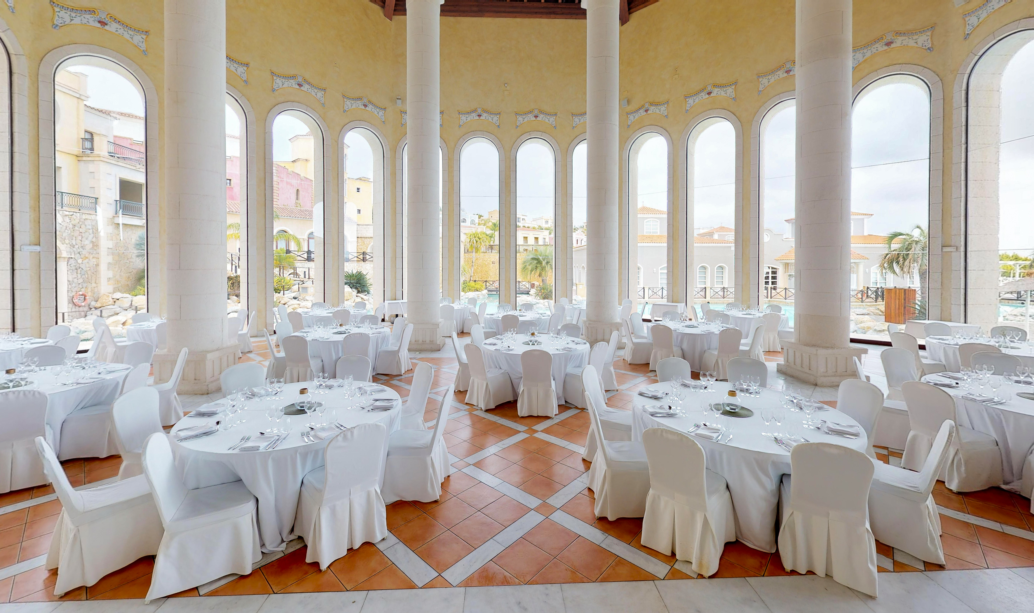 Elegant banquet hall with white tables, columns, and arched windows.