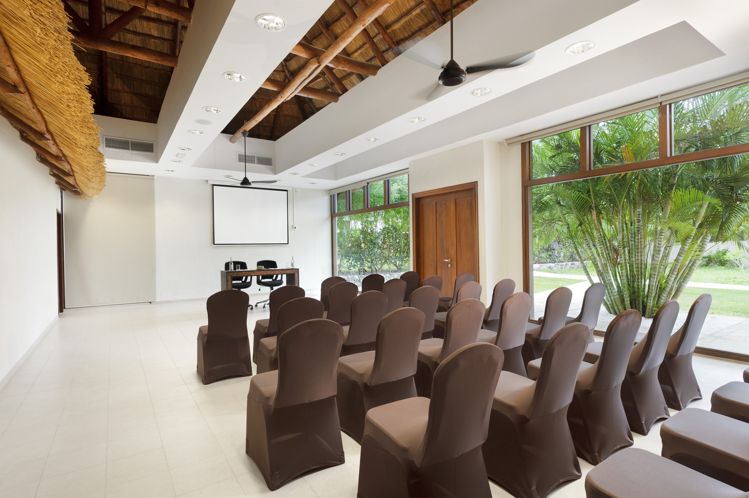Modern conference room with brown chairs, projector screen, and tropical views.