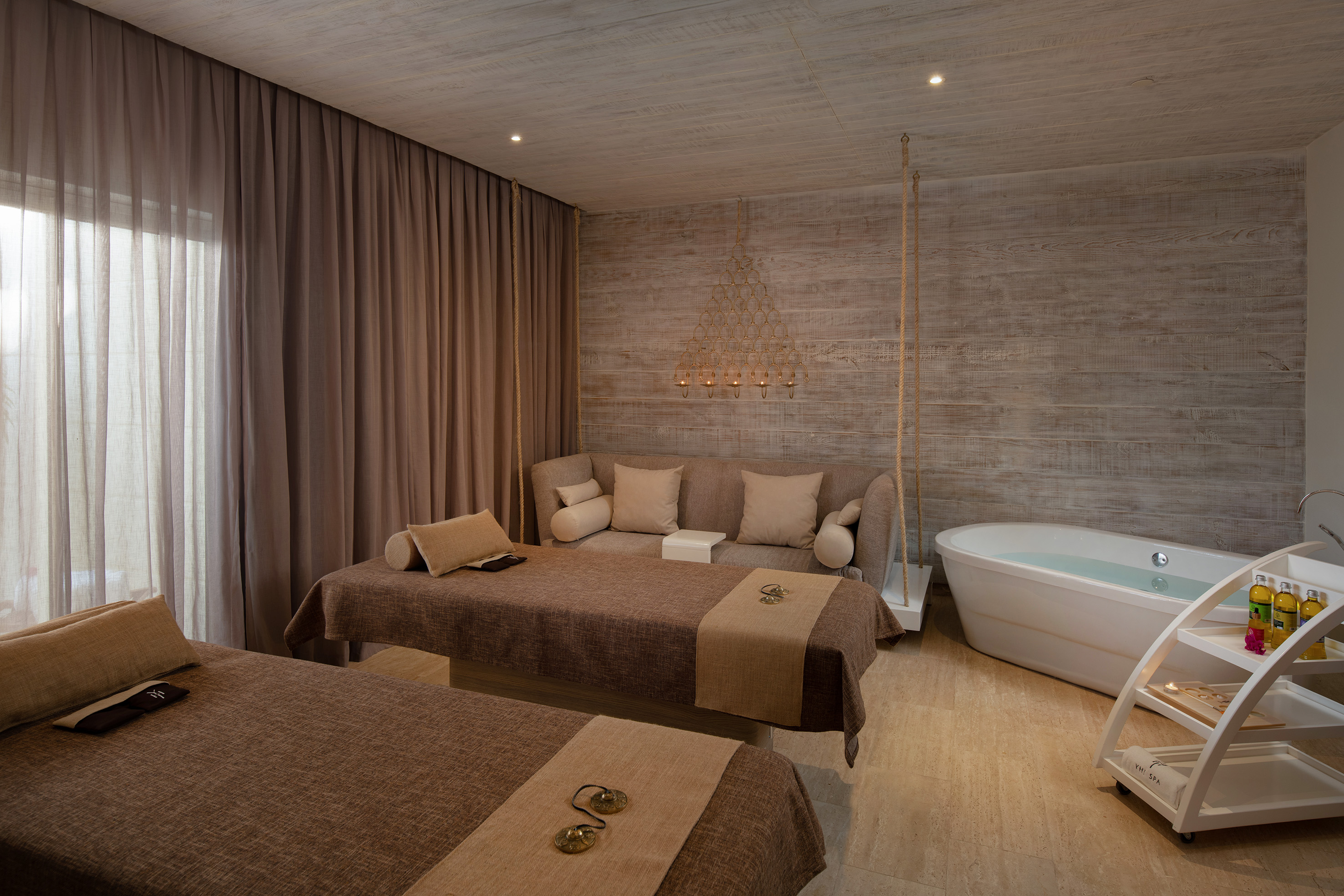 Luxury spa room with two massage beds, sofa, and freestanding bathtub.