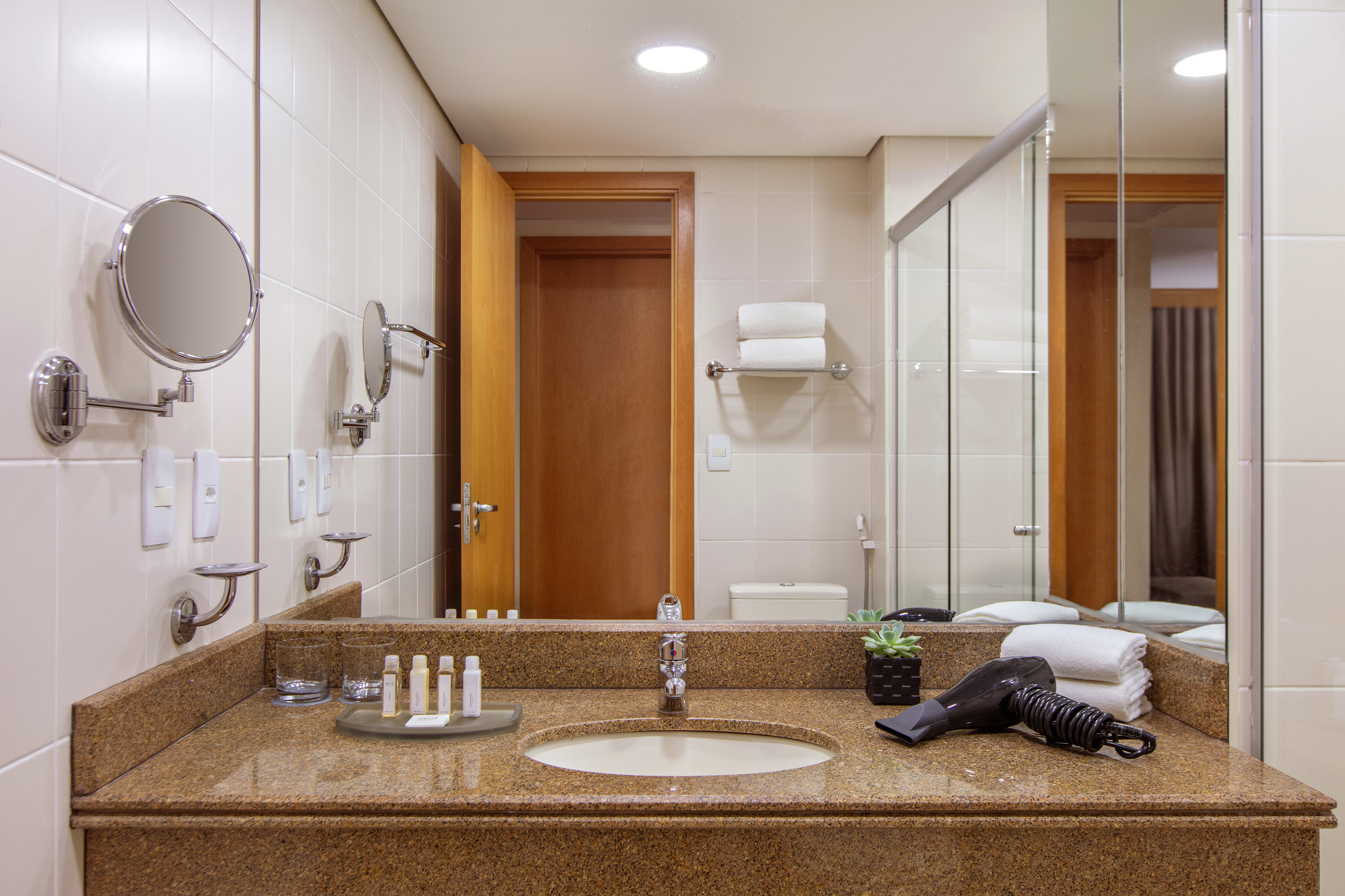 Hotel bathroom: granite vanity, sink, large mirror, toiletries, hairdryer, towels.