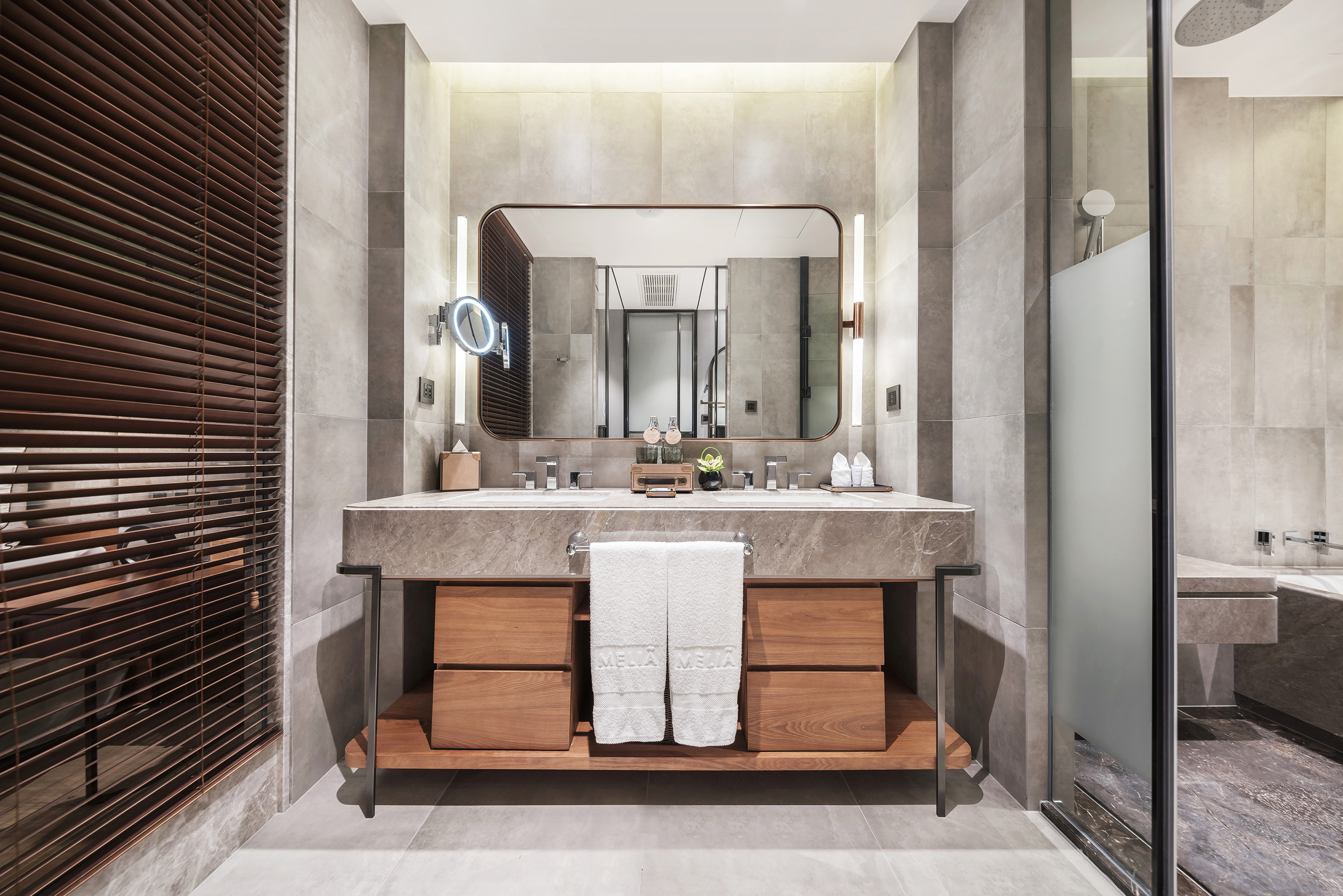 Contemporary double vanity bathroom, marble top, wood base, illuminated mirror.