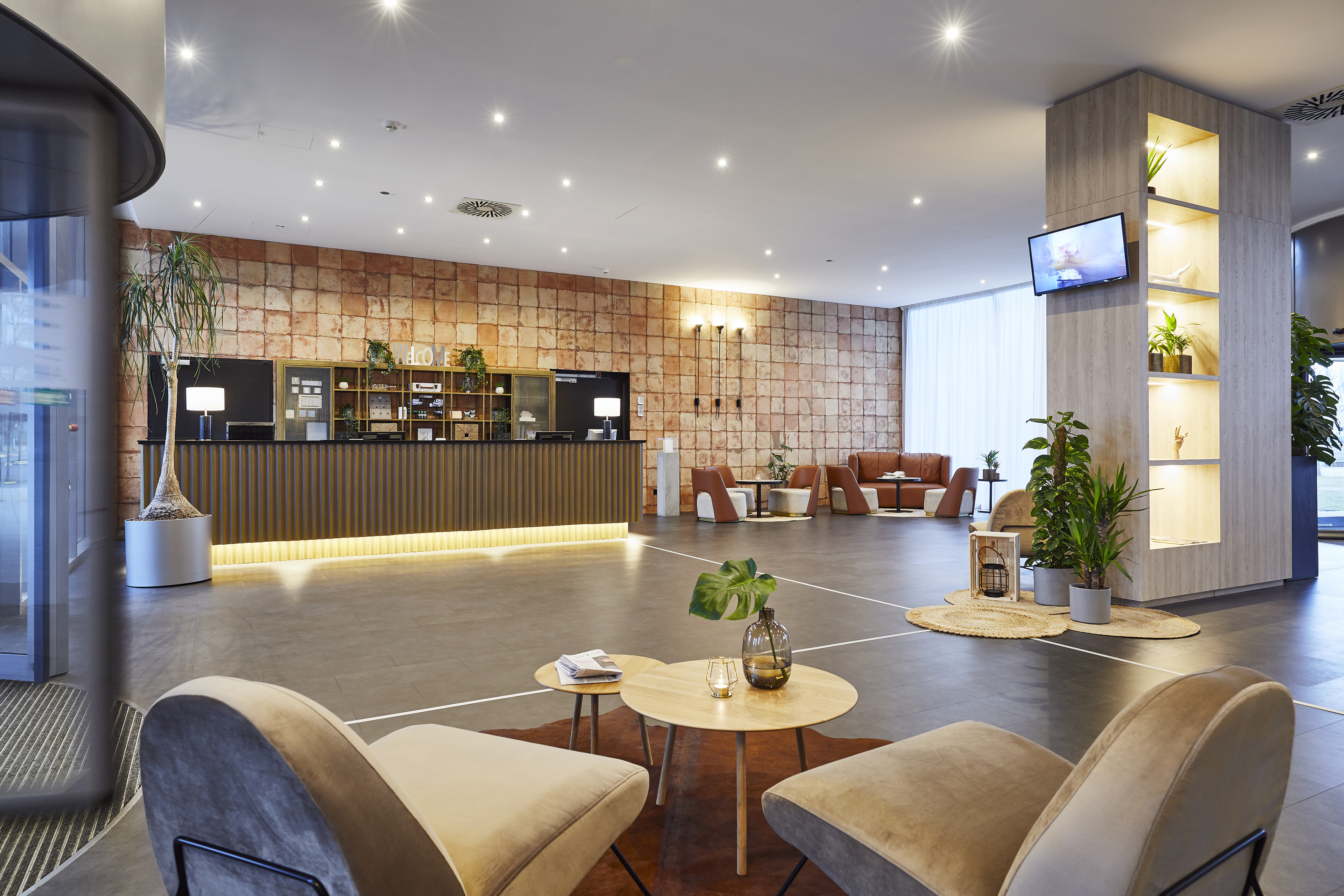 Modern hotel lobby with reception, lounge seating, and warm brick wall decor.