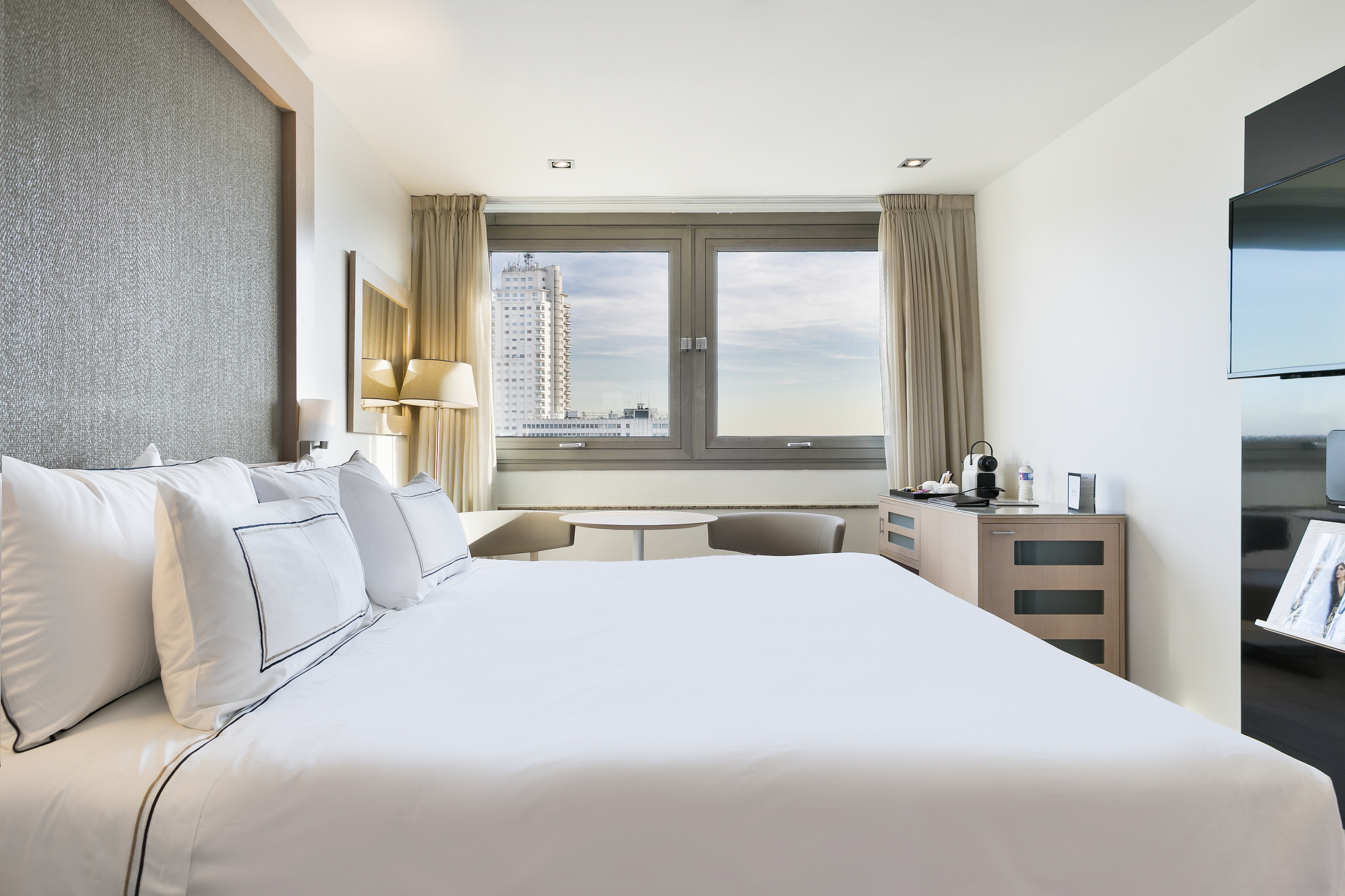 a bed with white sheets and pillows in a hotel room