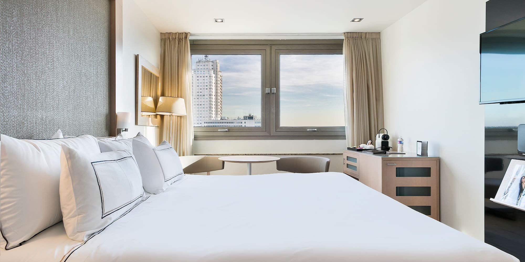 a bed with white sheets and pillows in a hotel room