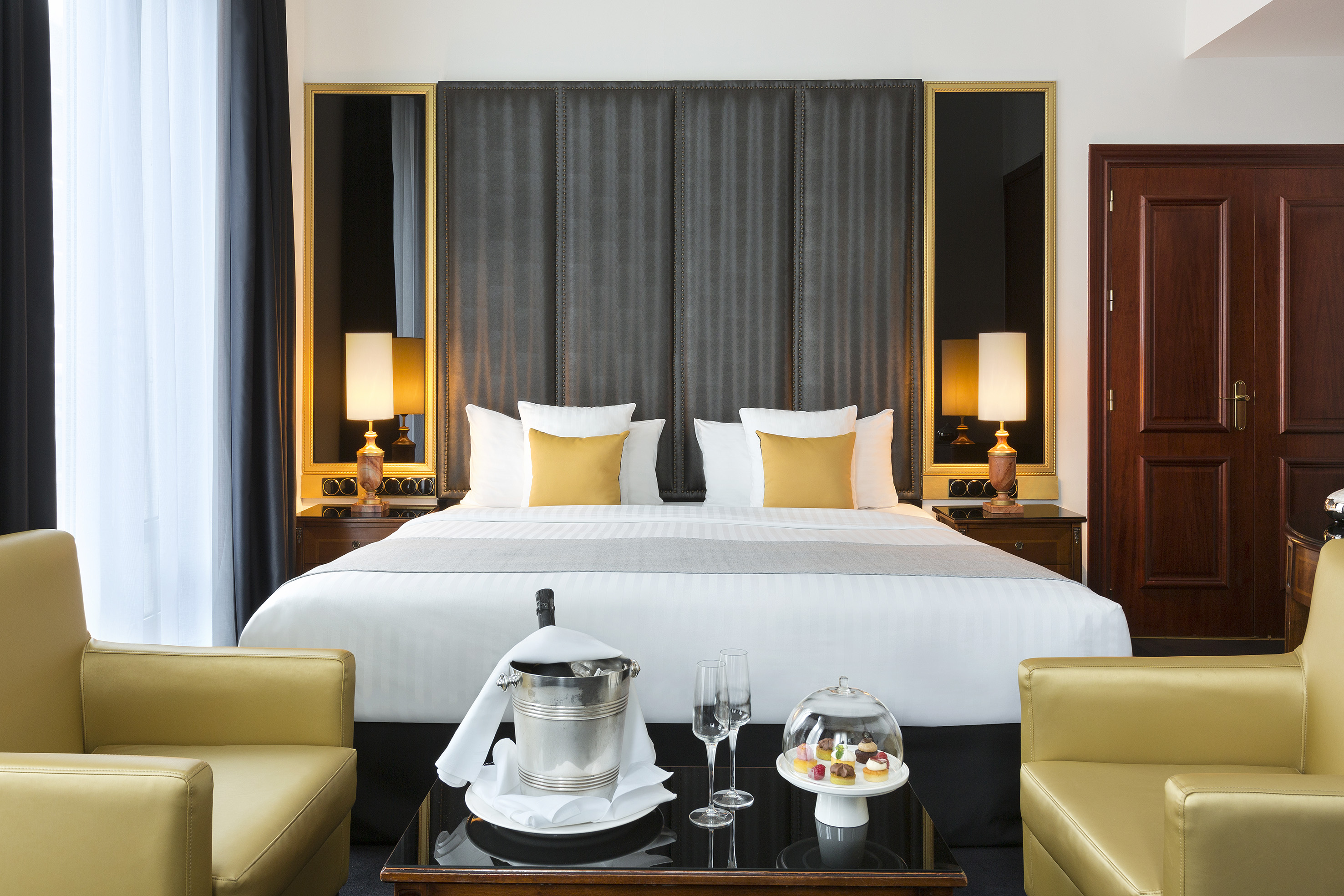 Elegant hotel bedroom with king bed, champagne, and sweet treats.