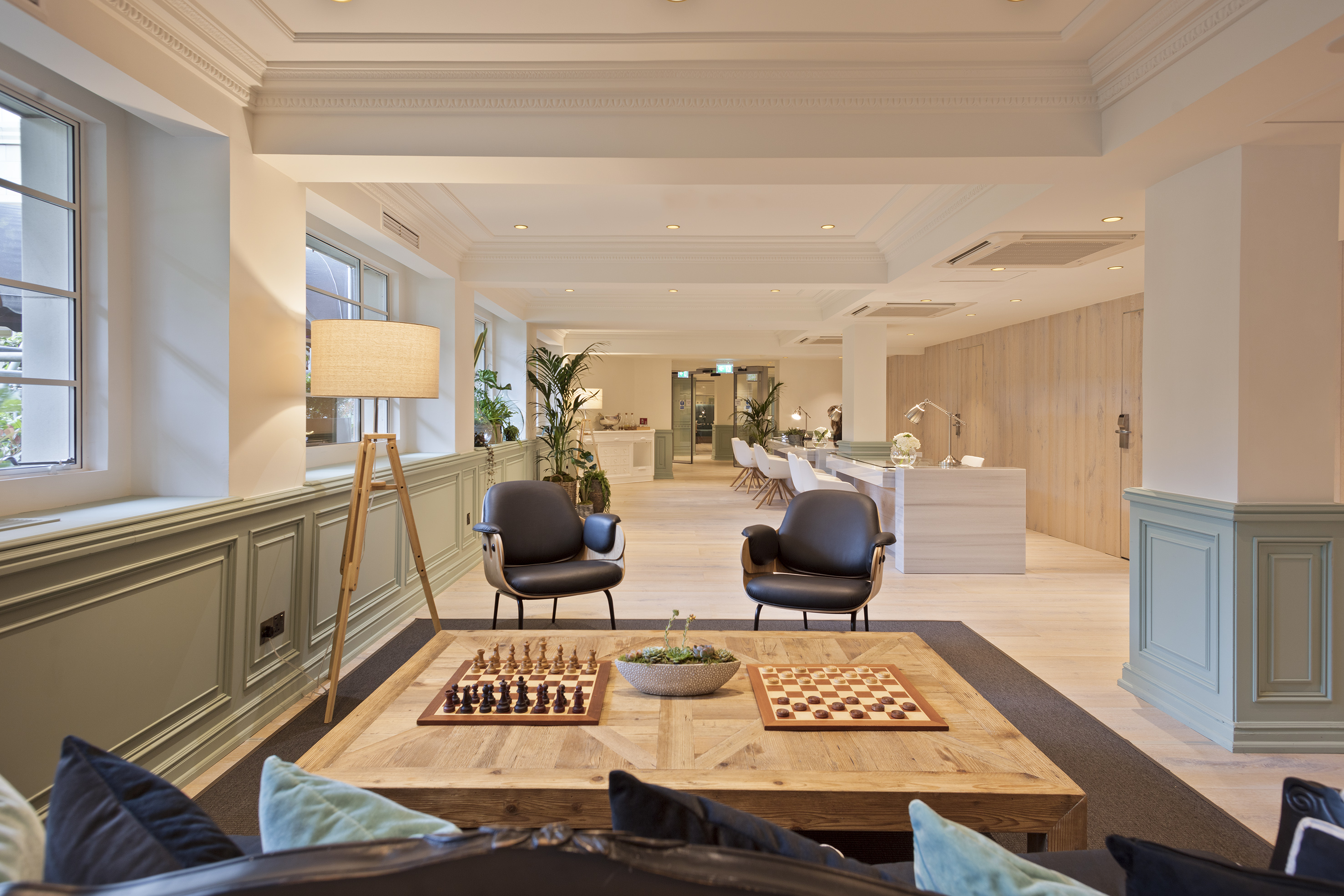 Modern hotel lounge with chess table, armchairs, and reception area.