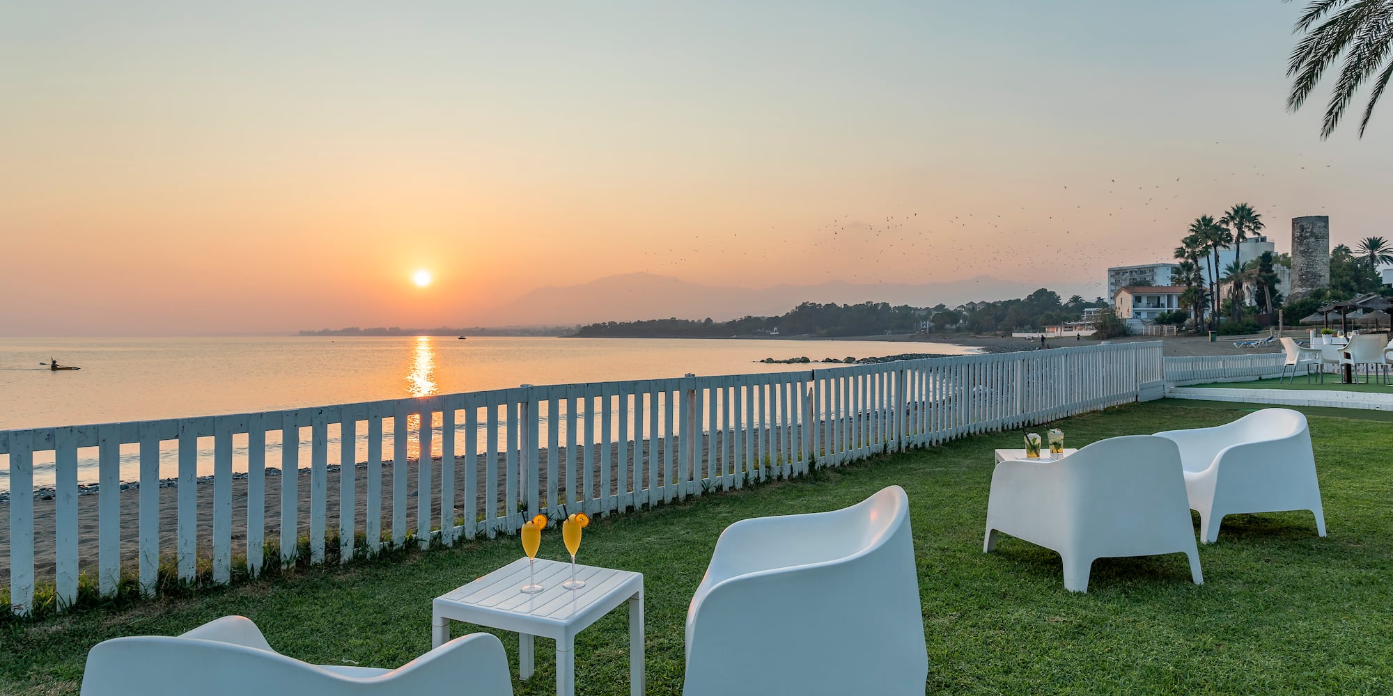 a lawn with white chairs and tables on it by a fence