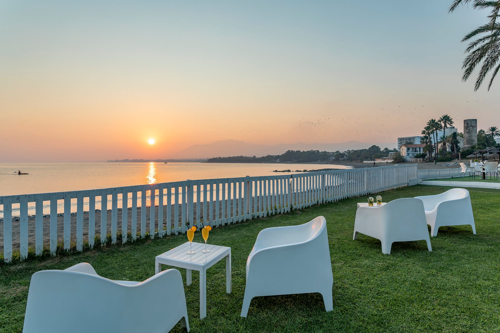 a lawn with white chairs and tables on it by a fence