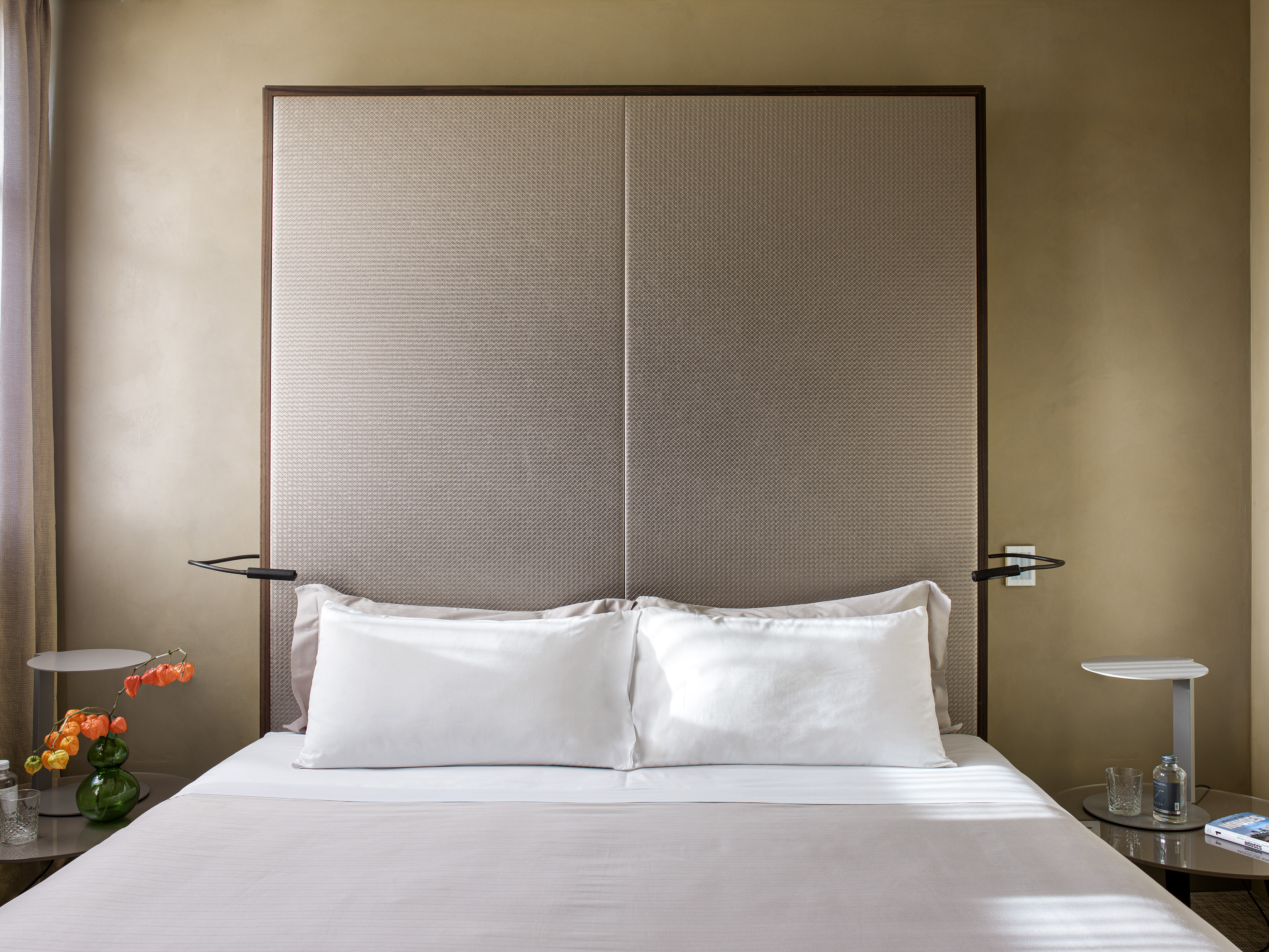 Modern hotel bedroom with neutral tones, textured headboard, and bedside tables.